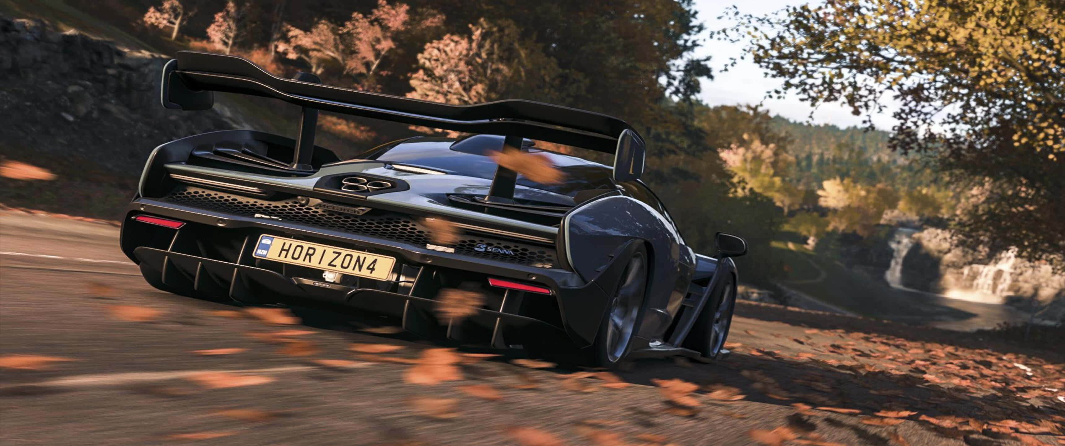 3440x1440p 黑色麥拉倫 Senna Forza Horizon 4 背景 壁紙 — 一輛黑色麥拿倫Senna在蜿蜒的森林道路上穿過秋葉，背景有瀑布。