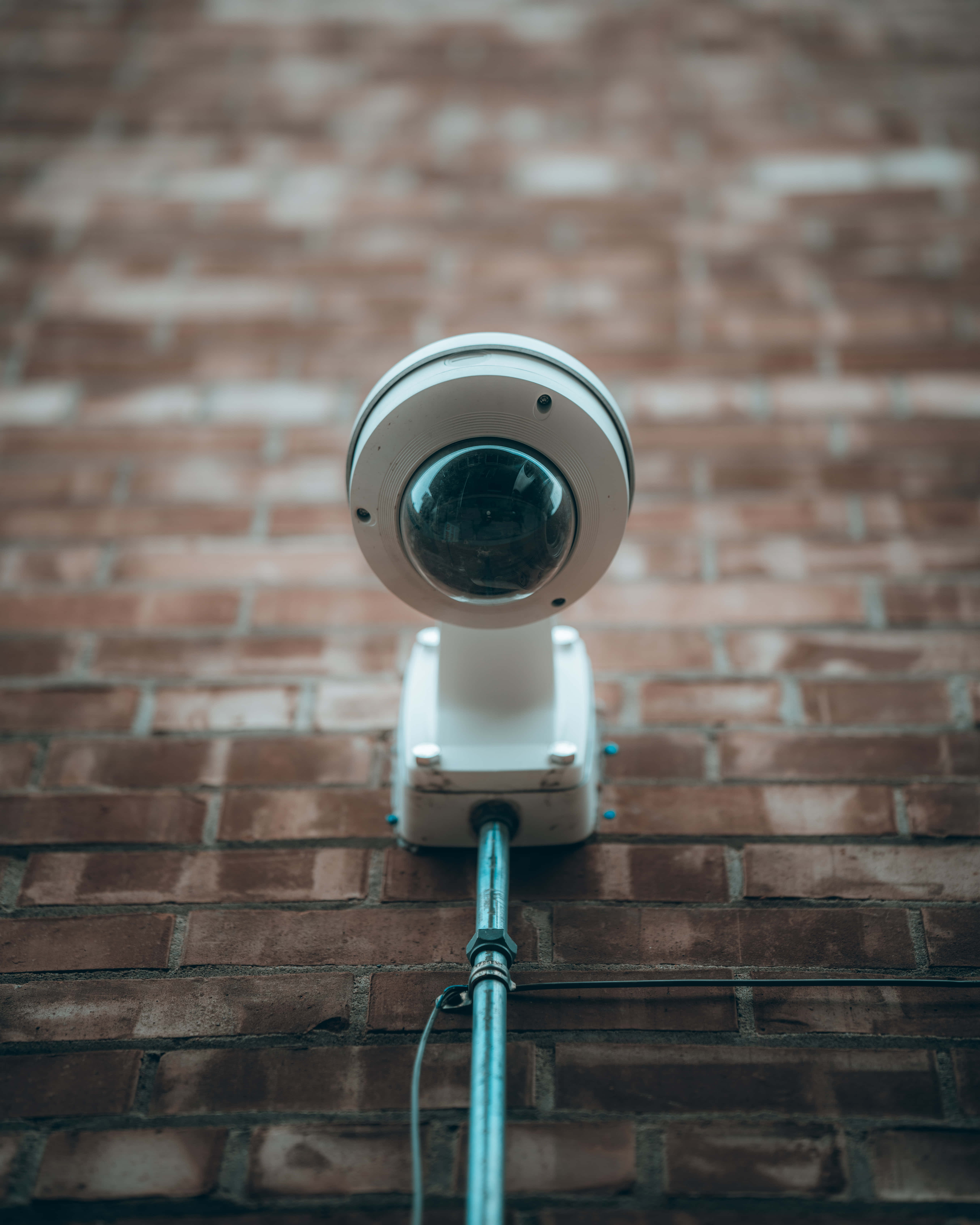360度穹頂安全攝像機運作中 壁紙 — 一個白色半球形安全攝像頭安裝在磚牆上，帶有金屬導管向下延伸。