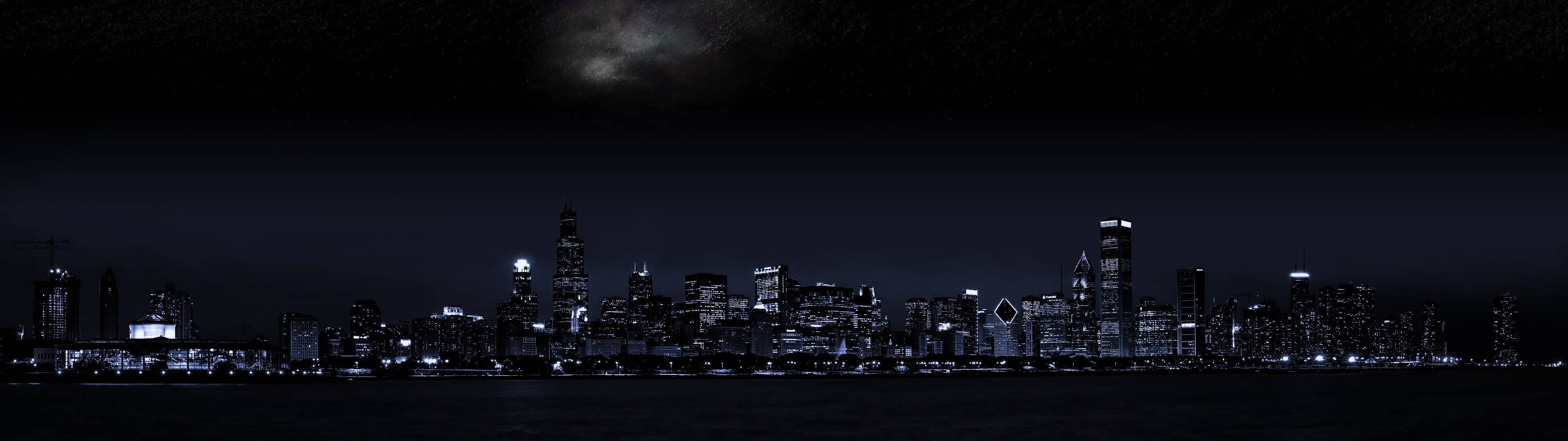 3840x1080 HD 雙螢幕夜景 壁紙 — 城市天際線的夜間全景，帶有發光的窗戶和上方陰暗多雲的天空。
