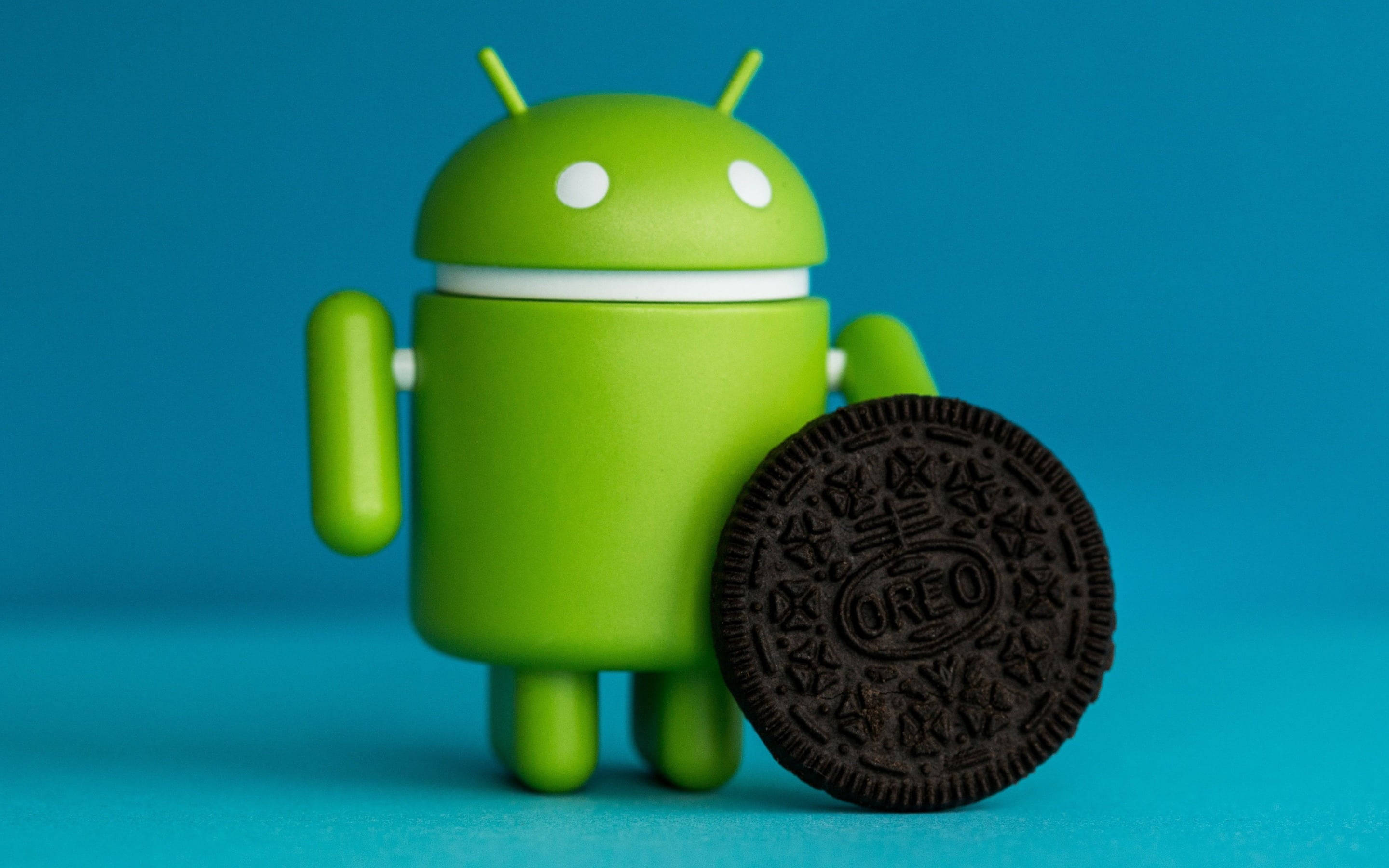 3D Android圖標與奧利奧桌面壁紙 壁紙 — 一個綠色Android公仔站在一塊朱古力Oreo曲奇旁邊，背景為純藍色。