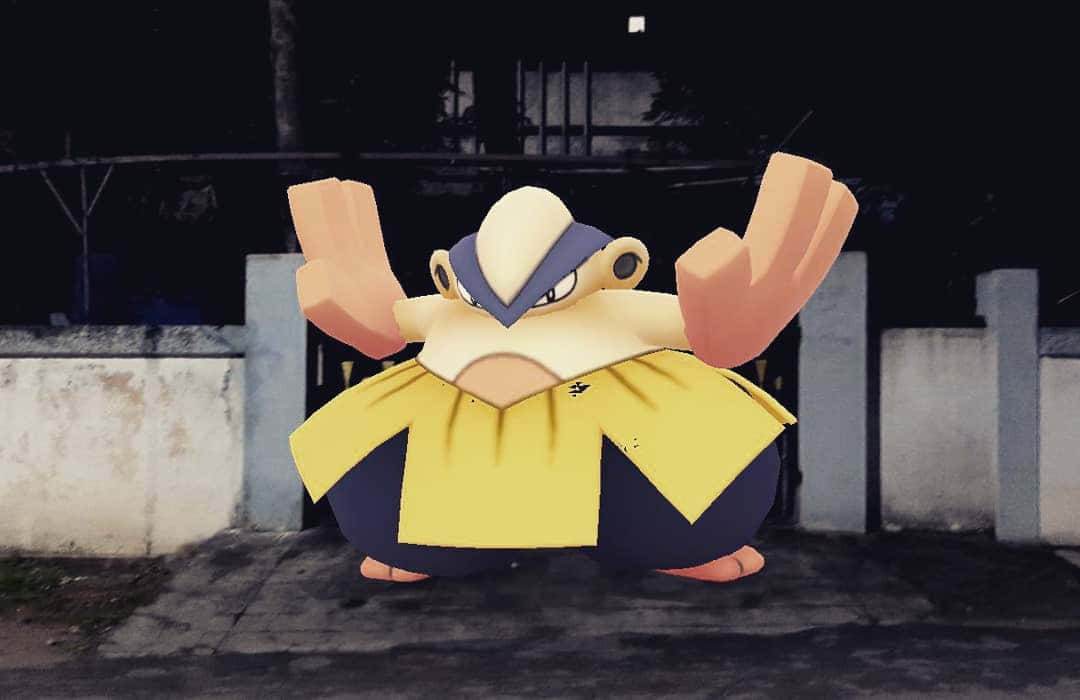 3D Hariyama 把守大門 壁紙 — 一隻巨大的動畫寶可夢，身穿黃色和藍色盔甲，在夜晚的黑暗城市小巷中舉起雙臂站立。
