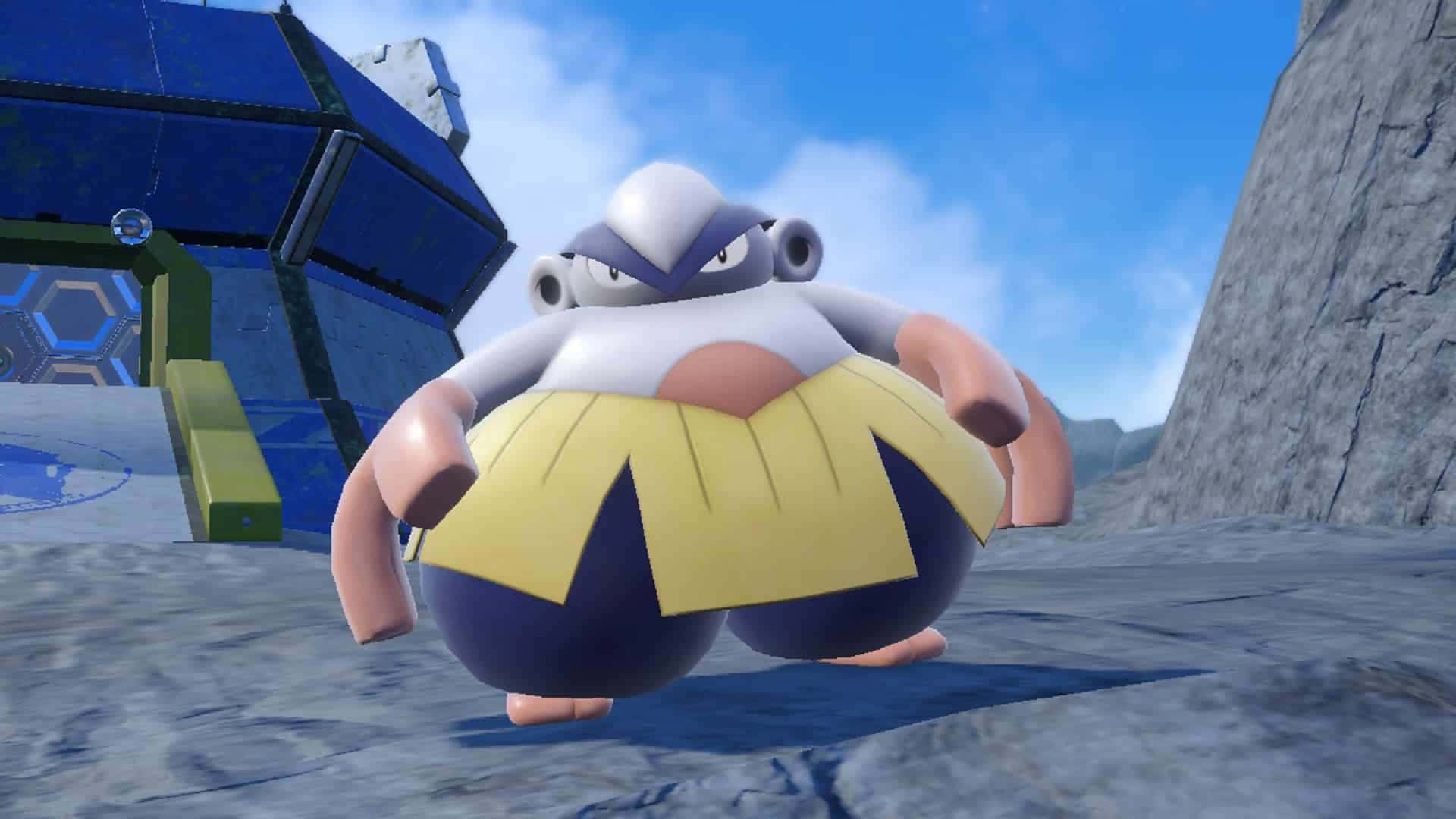 3D Hariyama 站立凝視鏡頭 壁紙 — 一隻體型龐大的寶可夢，穿著黃色裙子，白色頭部，站在岩石地形上，靠近一座未來主義的藍色建築，天空湛藍。