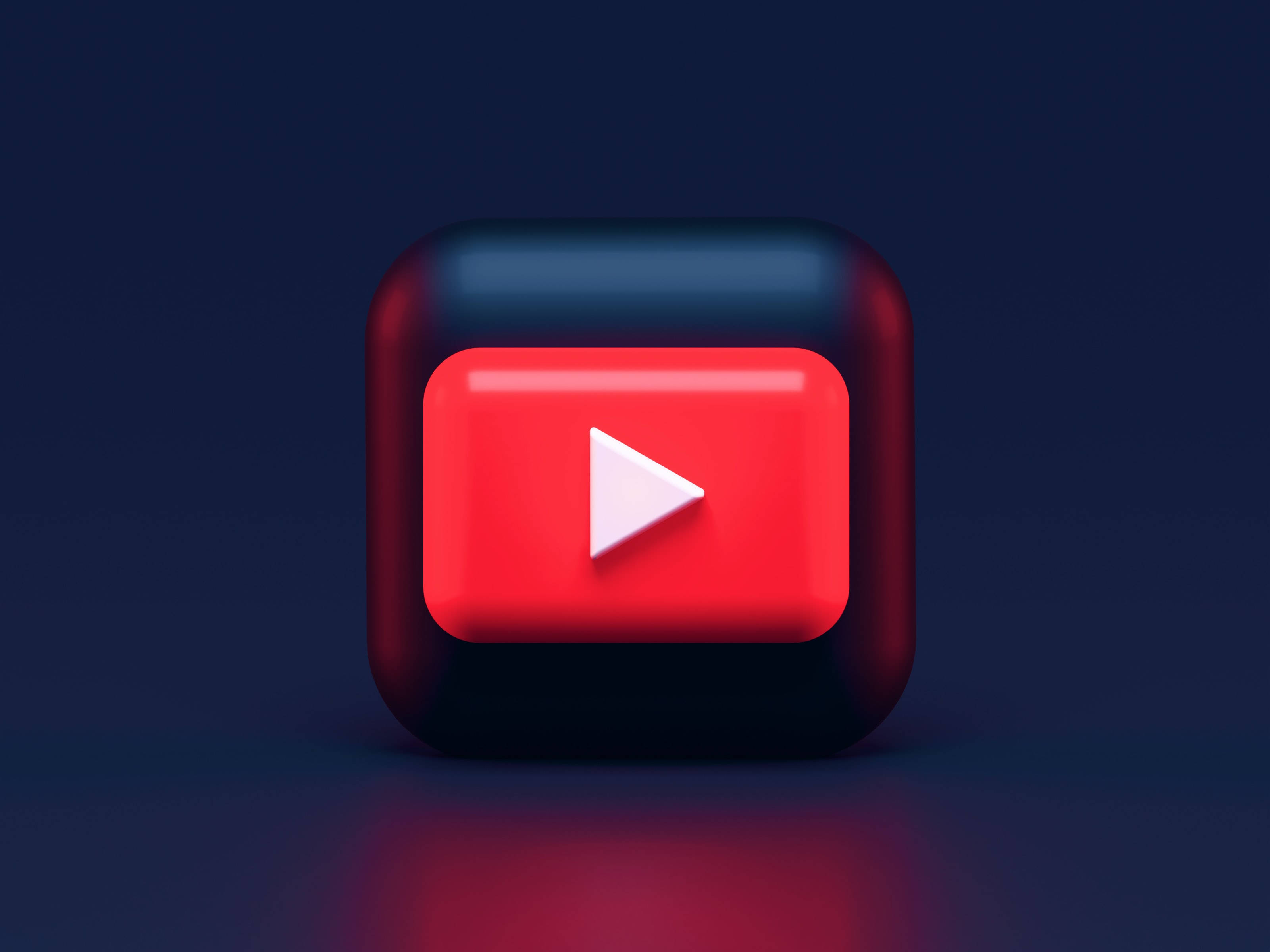 3D YouTube標誌動畫桌面 壁紙 — 一個帶有紅色和黑色漸變的光澤3D渲染YouTube播放按鈕圖標，背景為深藍色。
