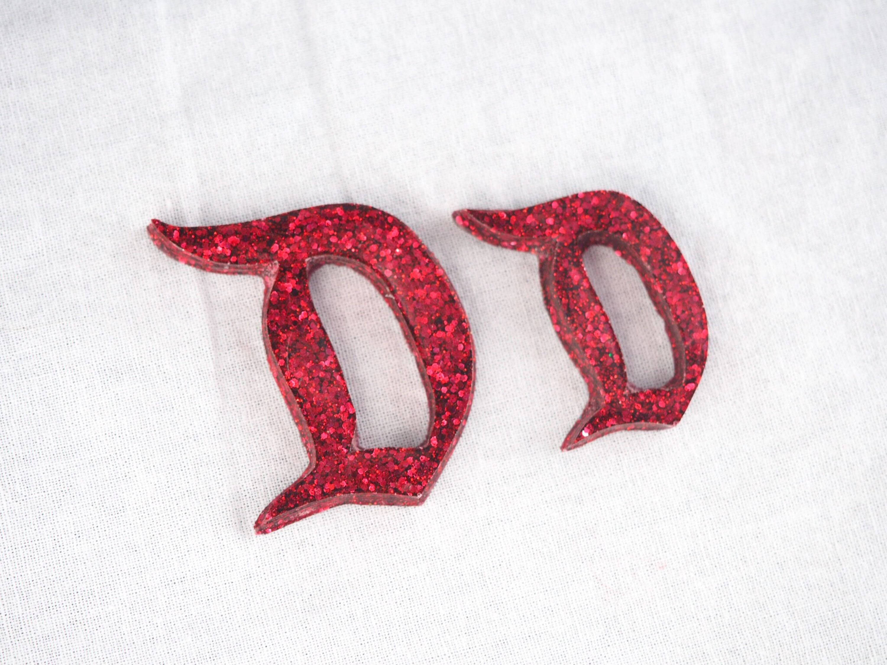 紅色3D草書字母D 壁紙 — 兩個大膽的紅色閃亮字母D放在柔軟的白色織物表面上，帶有紋理編織。