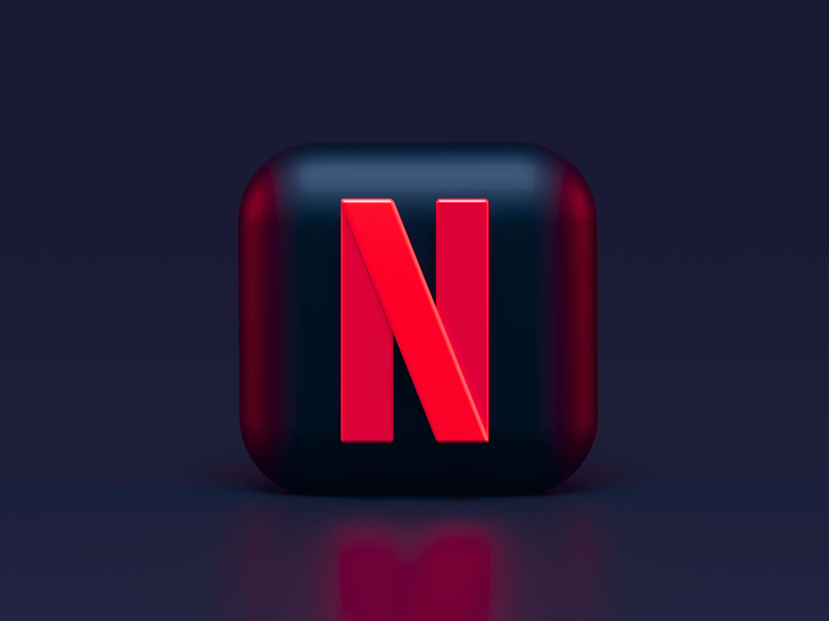 3D黑紅配色Netflix標誌背景 壁紙 — 一個光滑的黑色立方體，帶有醒目的紅色Netflix標誌，置於深色反光表面上，在柔和的工作室燈光下居中。
