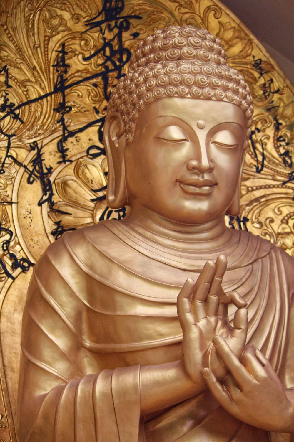 金色佛像雙手合十祈禱，背景是華麗的金色裝飾和書法。
