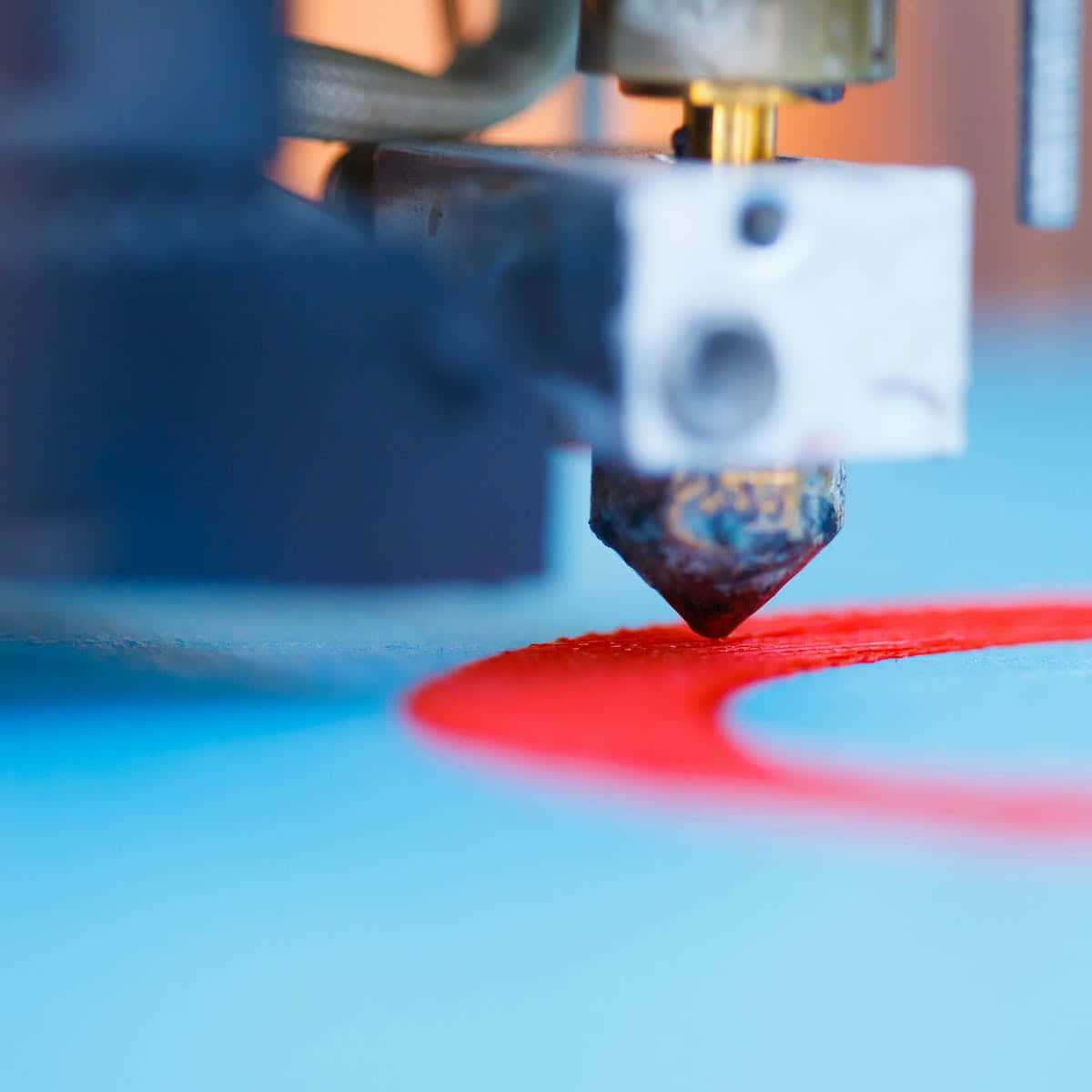 3d Printer 桌布 壁紙 — 3D打印機噴嘴將鮮紅色絲材擠出到光滑藍色表面上的特寫。