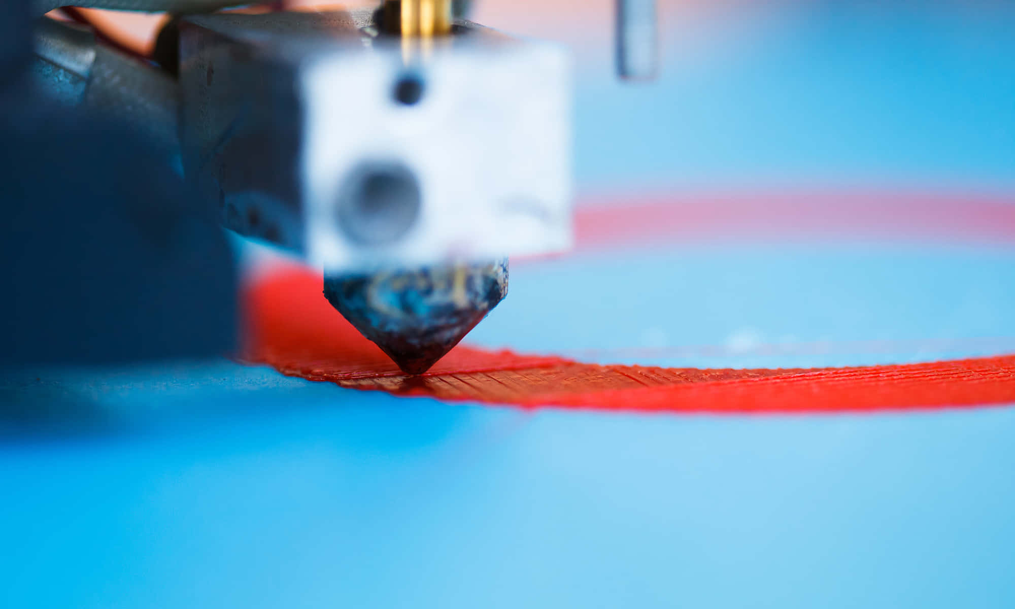3d Printer 桌布 壁紙 — 3D打印機噴嘴特寫，將鮮紅色燈絲擠出到藍色表面上，景深較淺。