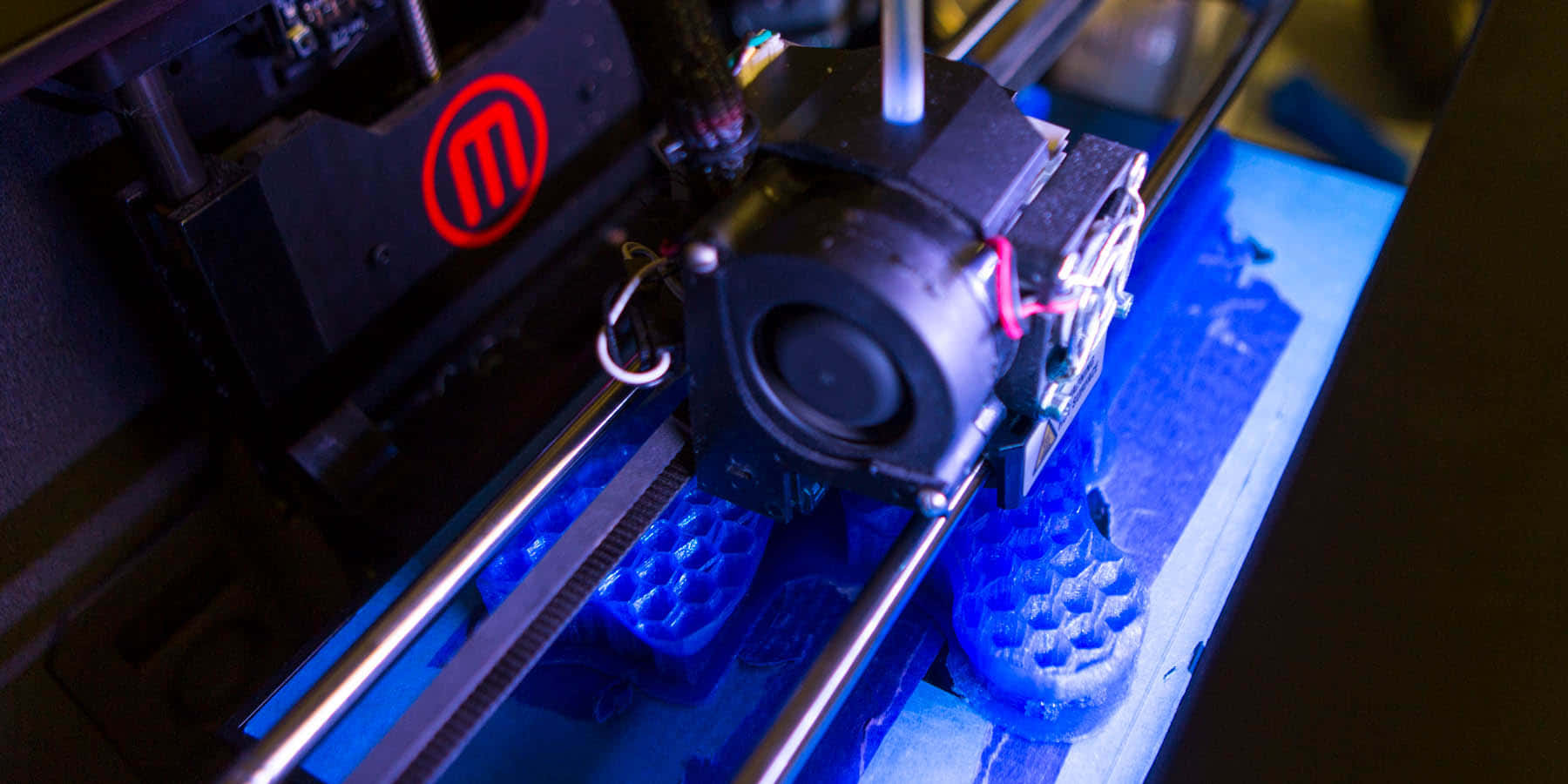 3d Printer 桌布 壁紙 — 3D打印機在昏暗燈光下將藍色線材擠出到構建板上的特寫。