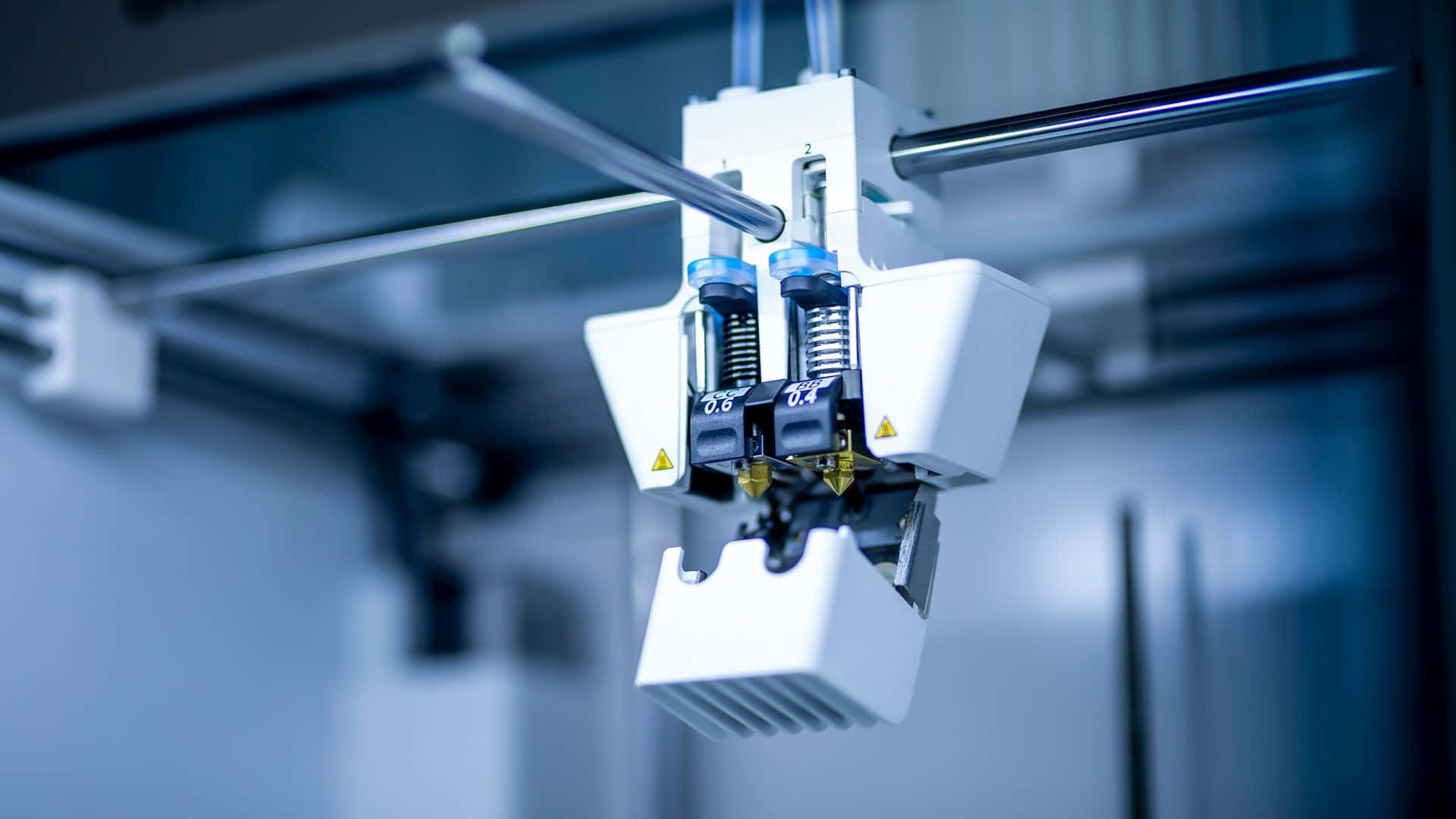 3d Printer 桌布 壁紙 — 3D打印機雙擠出頭的特寫，帶有藍色噴嘴和金色尖端，懸浮在涼爽的藍色工業環境中。