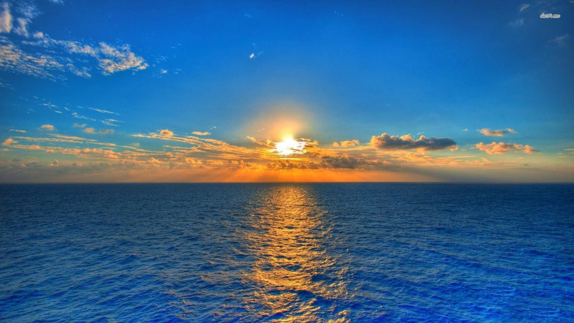 3D桌面海洋日落 壁紙 — 夕陽映照海洋，金色光芒穿透雲層，反射在深藍色的水面上。