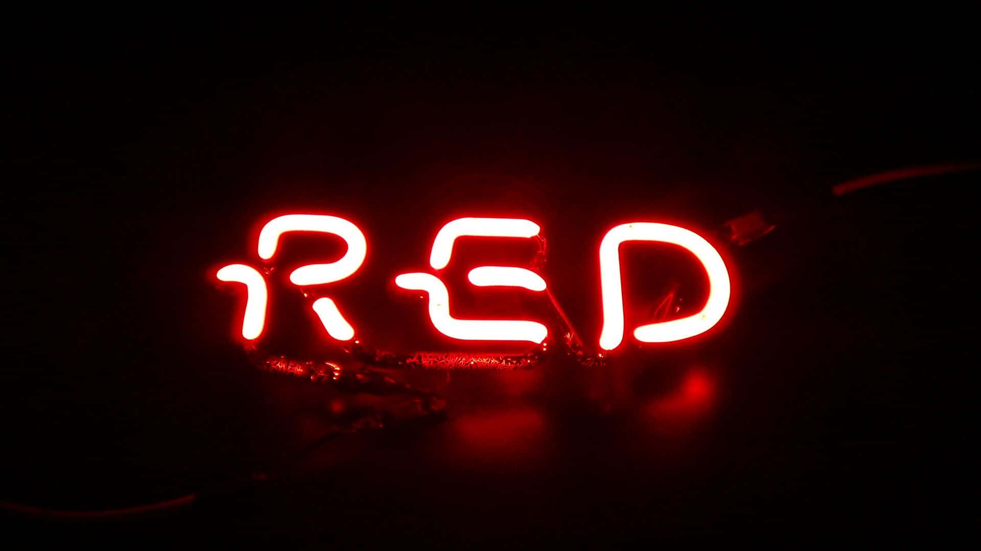 3D霓虹紅LED燈牌圖片 壁紙 — 一個發光的紅色霓虹燈牌，拼寫著 'RED'，在漆黑的背景上脈動，帶有可見的電線和反射。