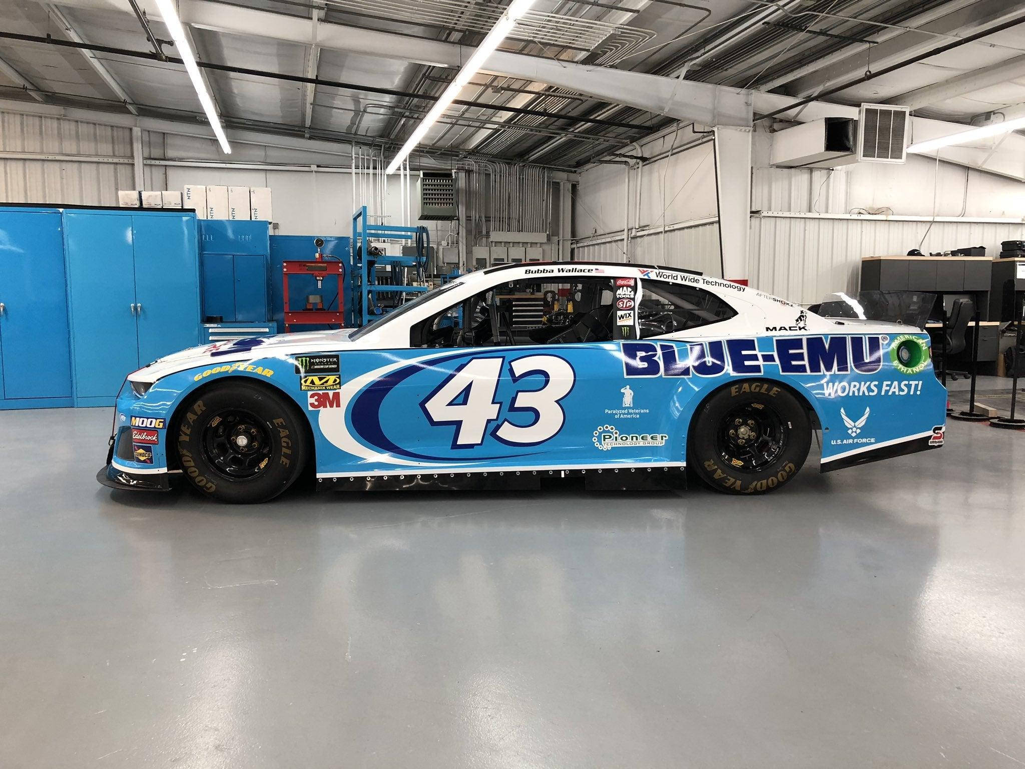 布巴·華盛頓藍色#43號NASCAR賽車停在車庫內 壁紙 — 一輛帶有「BLUE-EMU」品牌標誌的藍白#43 NASCAR賽車停放在光線充足的車庫內。