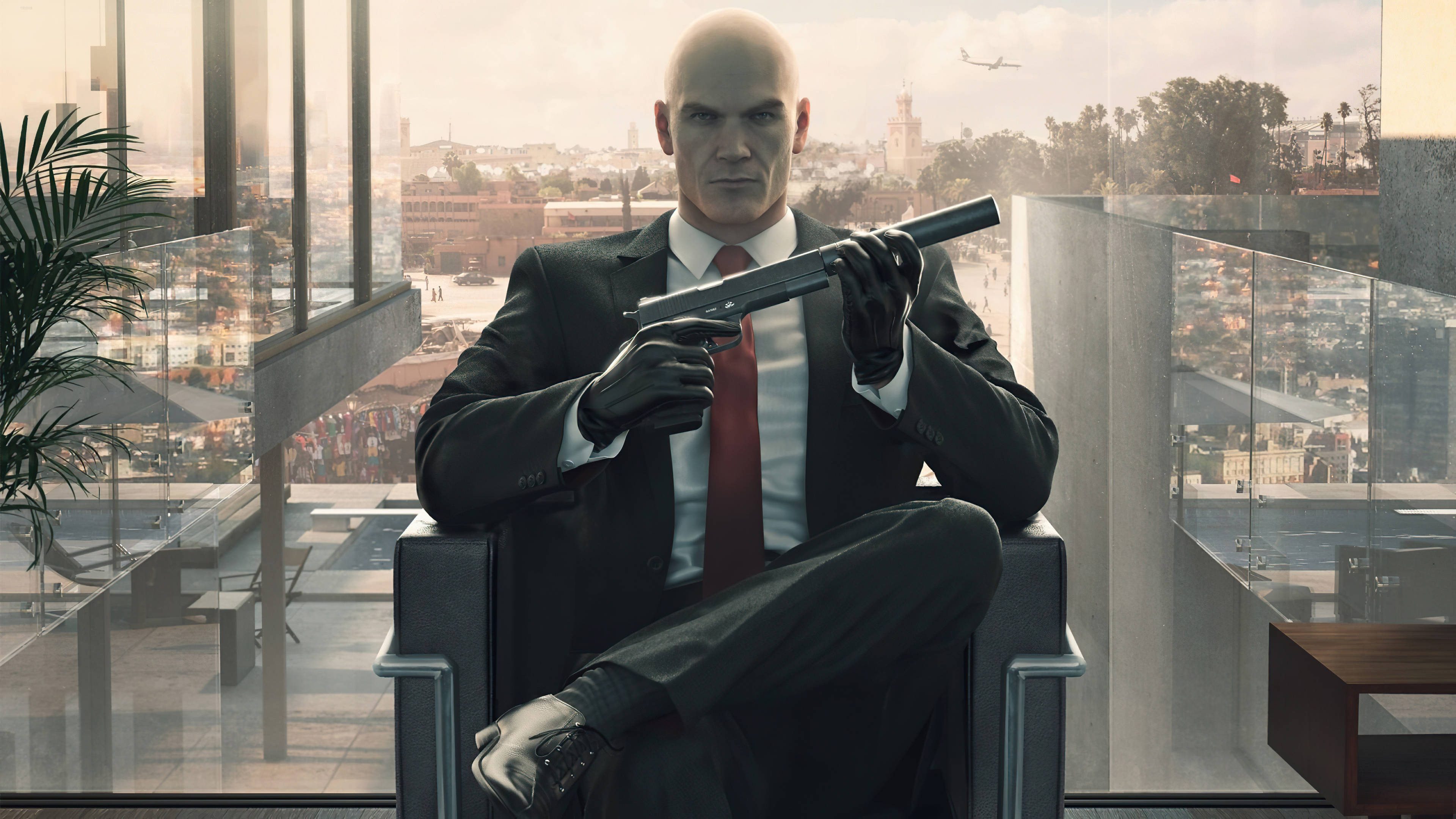 殺手47 - Hitman Phone 壁紙 — 一個光頭男子身穿西裝，坐在現代玻璃牆辦公室裡，手持消音手槍，俯瞰廣闊的城市景觀。
