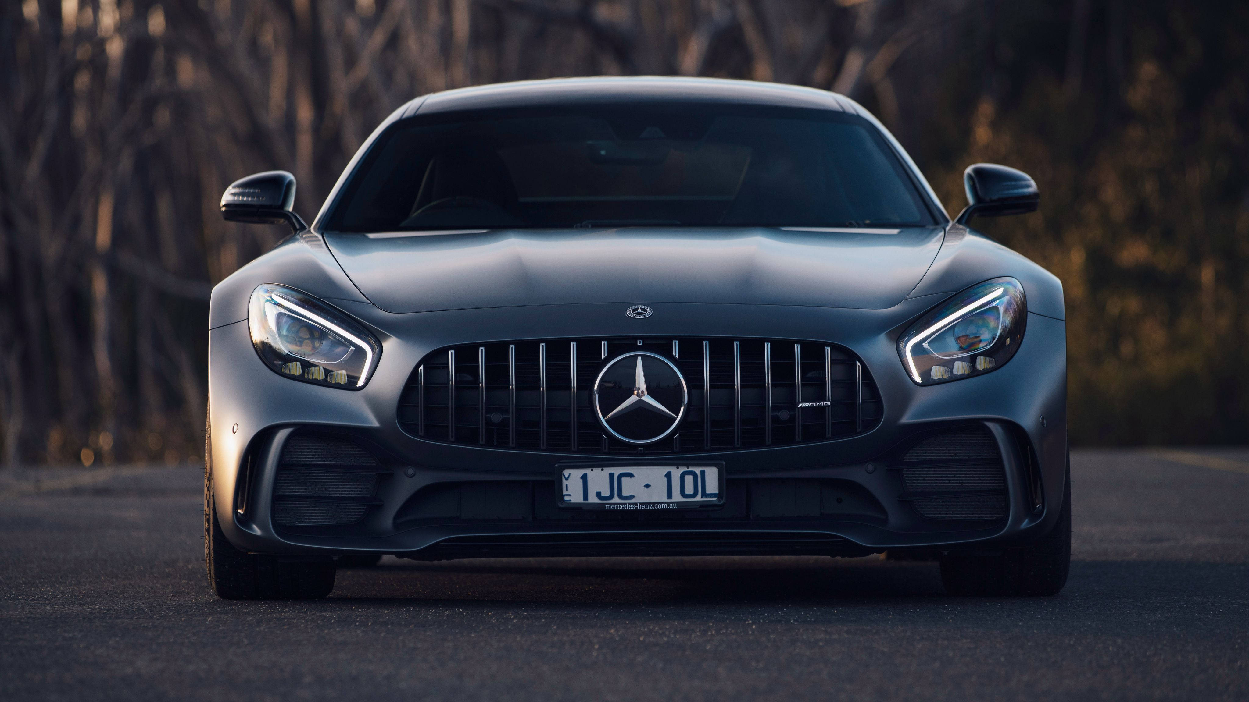 4K 2018 年梅賽德斯轎車 壁紙 — 一輛時尚的啞光灰色梅賽德斯-AMG GT跑車在道路上向前行駛，背景有模糊的樹木。