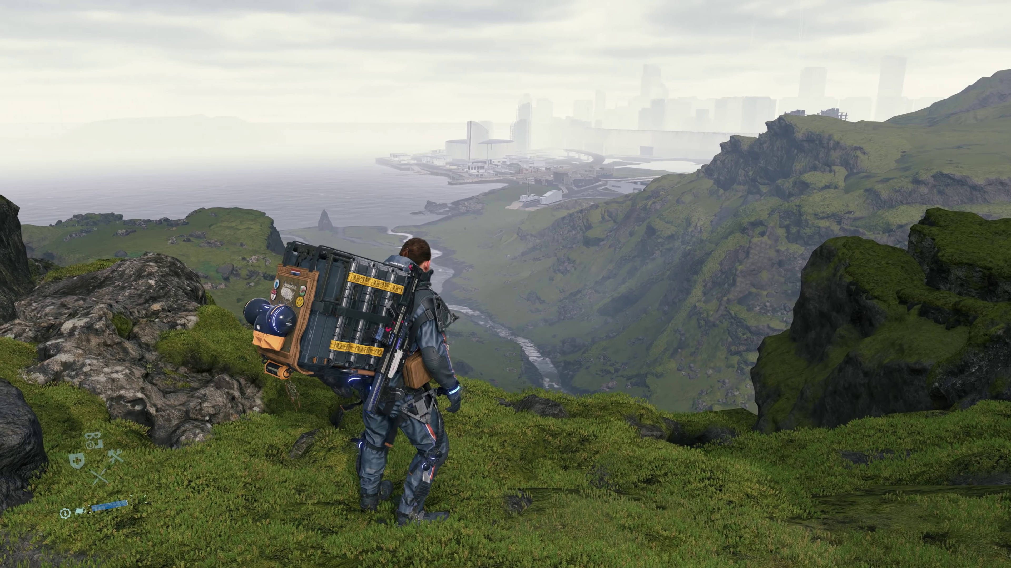 山姆山頂俯瞰《死亡擱淺》4K 壁紙 — 一個孤獨的探險家背著沉重的裝備包，站在霧氣瀰漫的綠色懸崖上，俯瞰遠處的未來城市景觀。