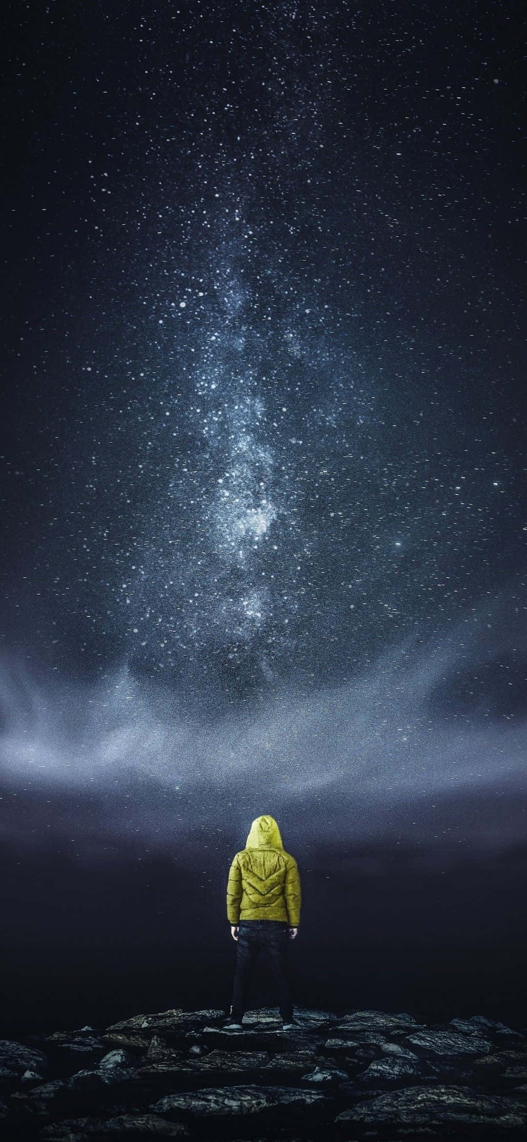 仰望星空男孩數位藝術 4K 壁紙 — 一個孤獨的人穿著黃色連帽外套站在岩石懸崖上，仰望令人嘆為觀止的星空，銀河在頭頂閃耀。