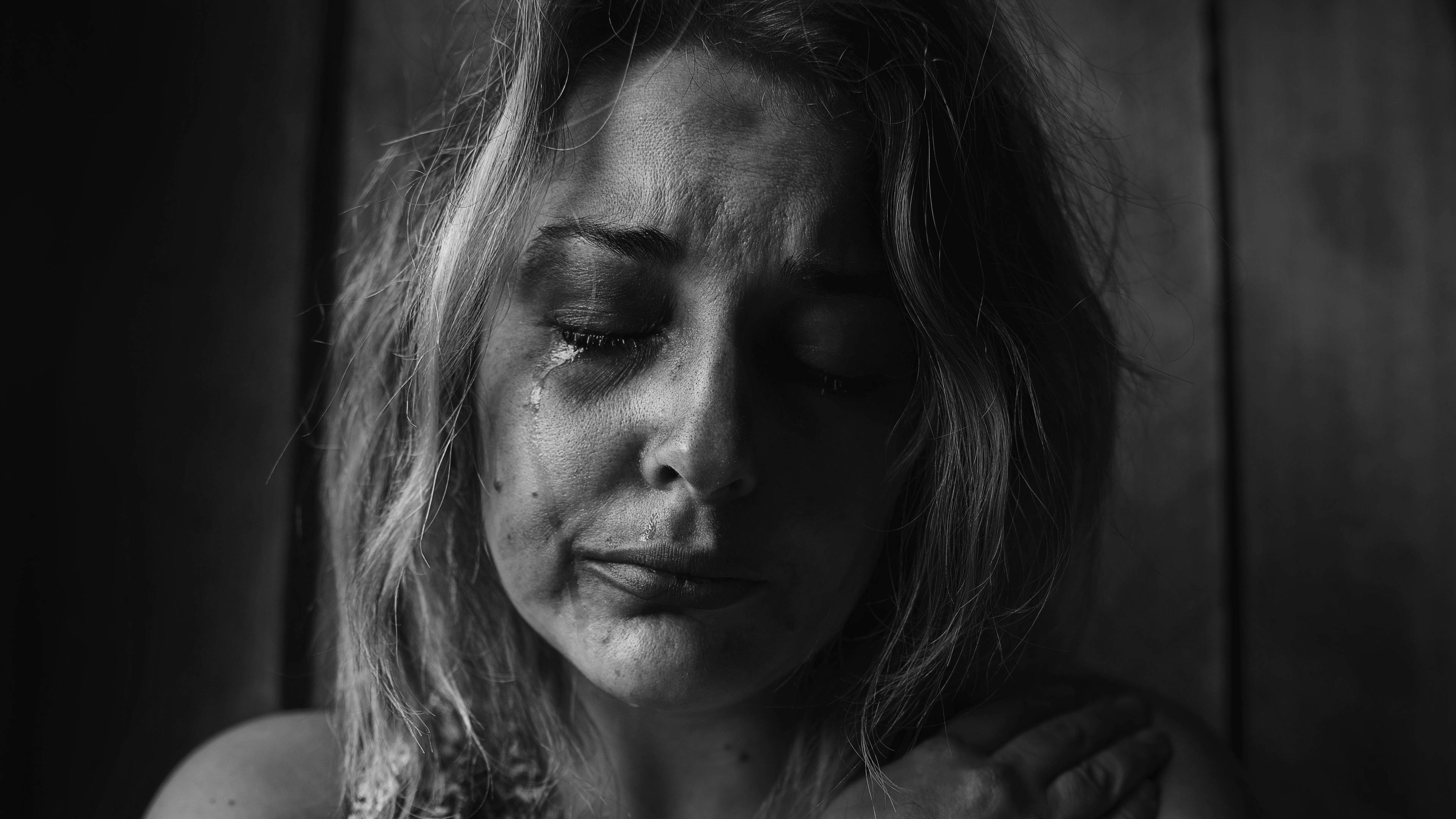 哭泣女子 4K 壁紙 — 一個黑白特寫鏡頭，一個女人閉著眼睛，淚水順著臉頰流下，背景是深色木質。