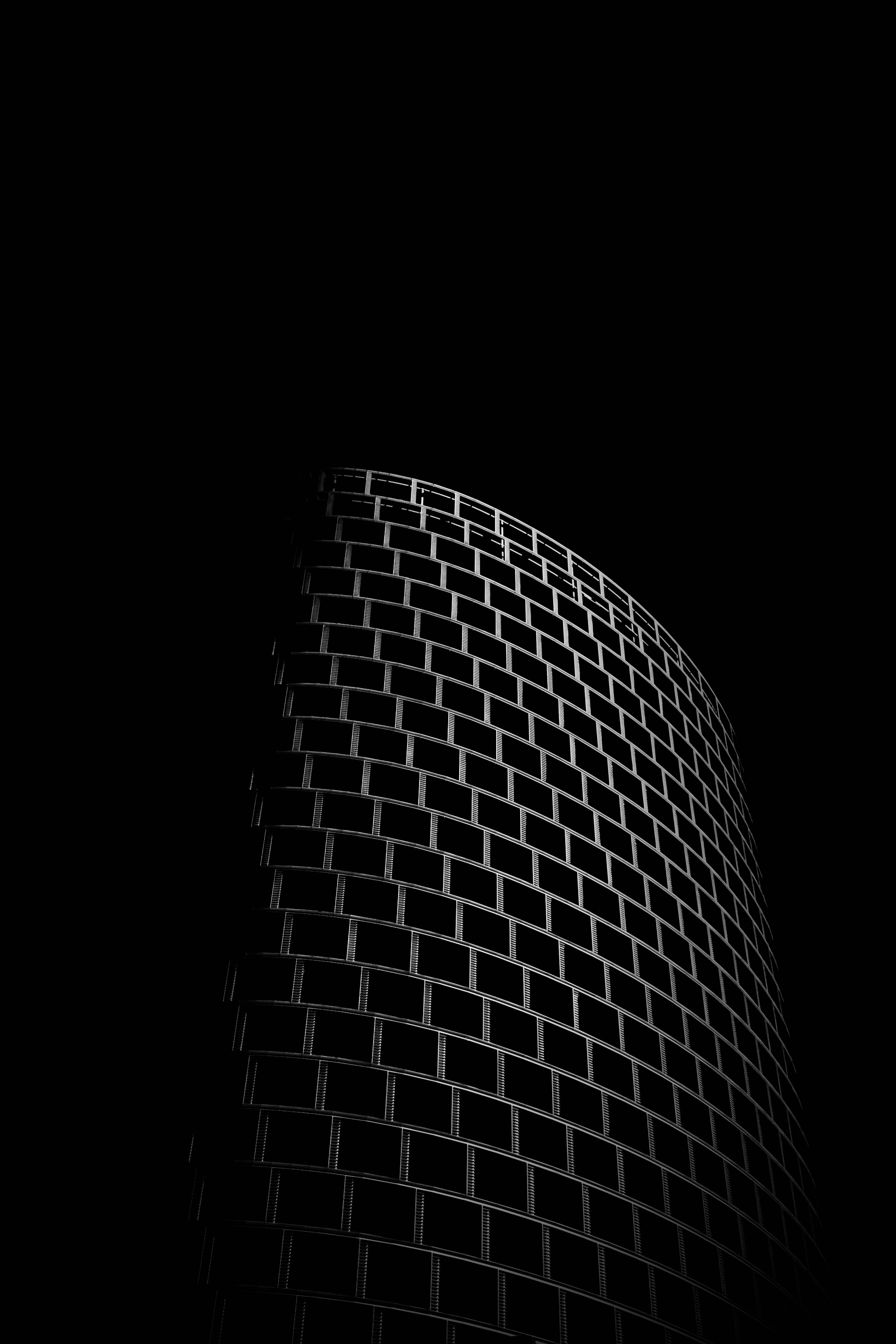 黑暗中的高塔 4K 黑底壁紙 壁紙 — 一幅清晰的黑白低角度照片，拍攝彎曲玻璃摩天大樓，背景是漆黑的天空。