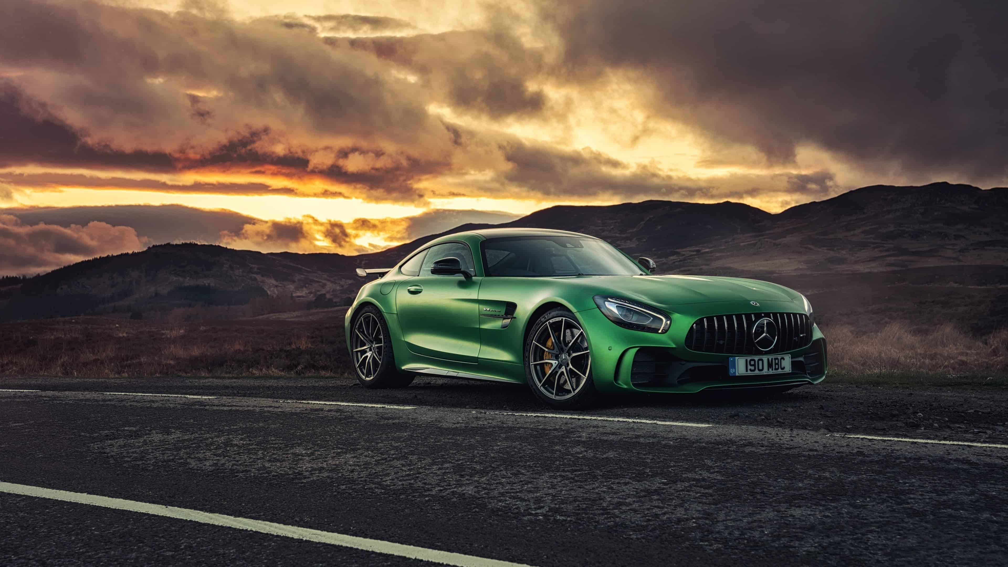 4K 梅賽德斯-奔馳綠色 AMG GT R 壁紙 — 一輛鮮綠色嘅Mercedes-AMG GT停喺日落時分嘅蜿蜒道路上，背景有戲劇性嘅雲層同起伏嘅山丘。
