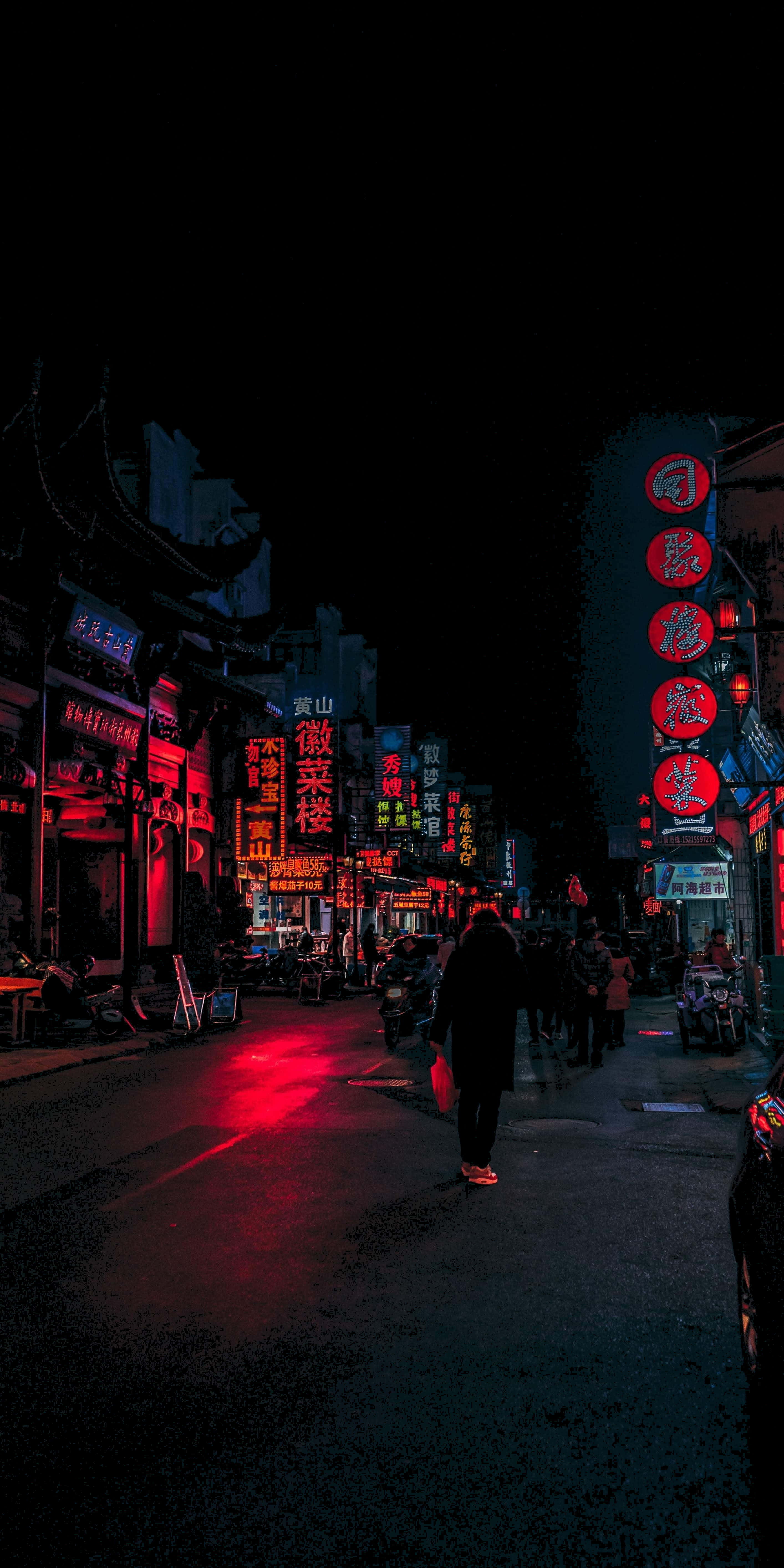 4K AMOLED 背景：夜間日本街景 壁紙 — 一個孤獨的身影在夜晚走下一條霓虹燈照亮的小巷，發光的紅色招牌映照在濕漉漉的路面上。