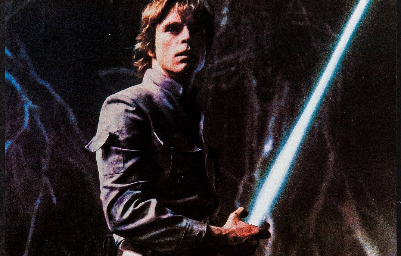 傳奇雷克·天行者 4K 解析度 壁紙 — Luke Skywalker 在黑暗洞穴中手持發光的藍色光劍，帶有戲劇性的燈光和強烈的表情。