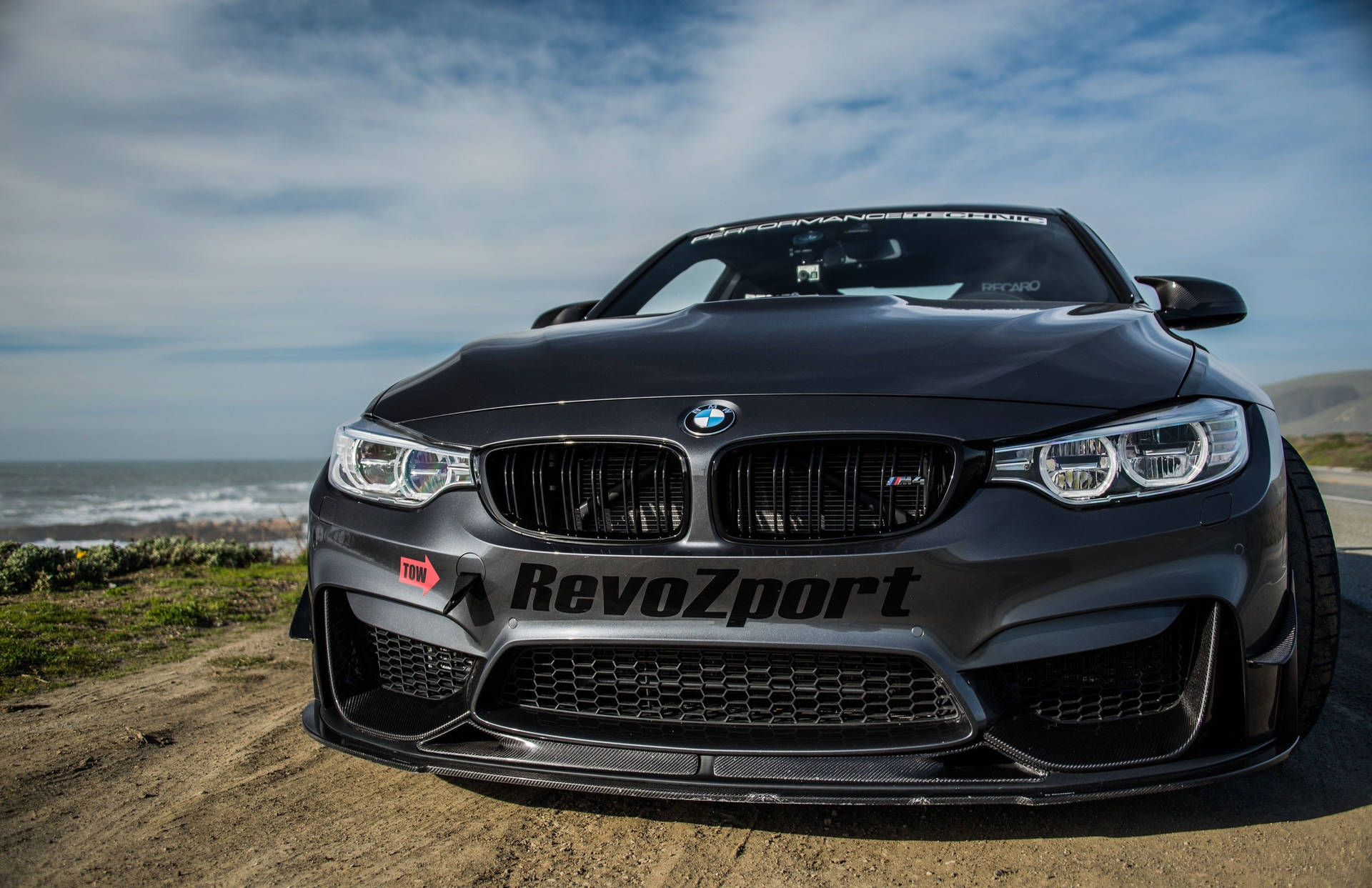 啞光黑色BMW M4性能車停泊在靠近海洋的沿海泥路上。 — 4K BMW 壁紙 壁紙