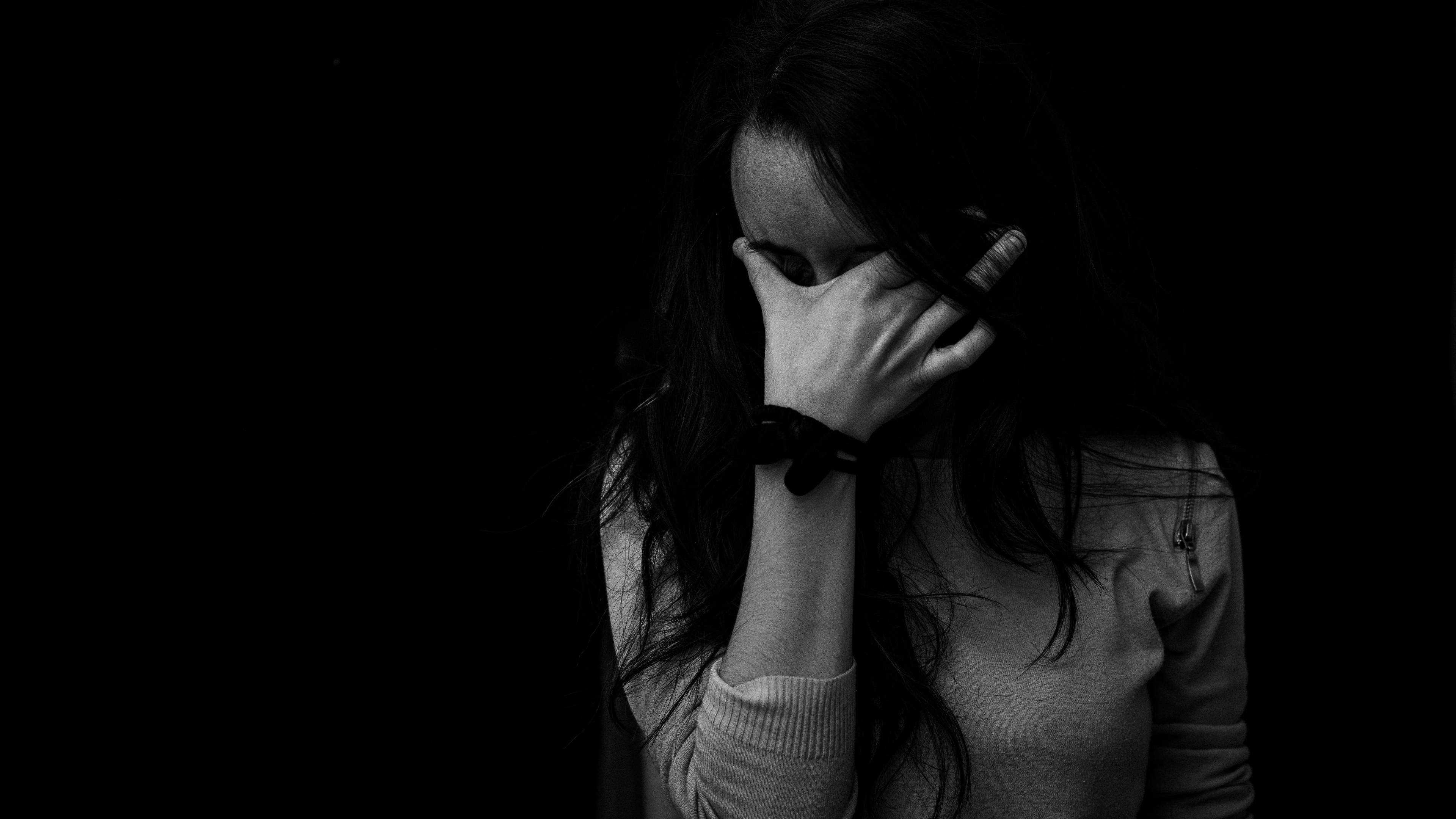 女子拭淚悲傷4K壁紙 壁紙 — 一位黑白女性在黑暗背景下用手遮住臉。