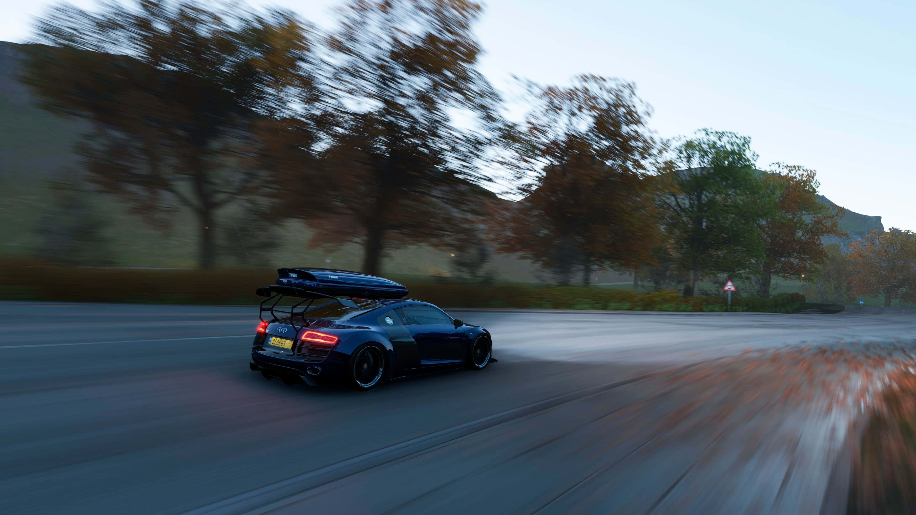 4K《Forza Horizon 4》背景：黑色車輛行駛於道路 壁紙 — 一輛流線型黑色跑車在秋季樹木間蜿蜒的道路上疾馳，帶有模糊的動態和柔和暮色燈光。