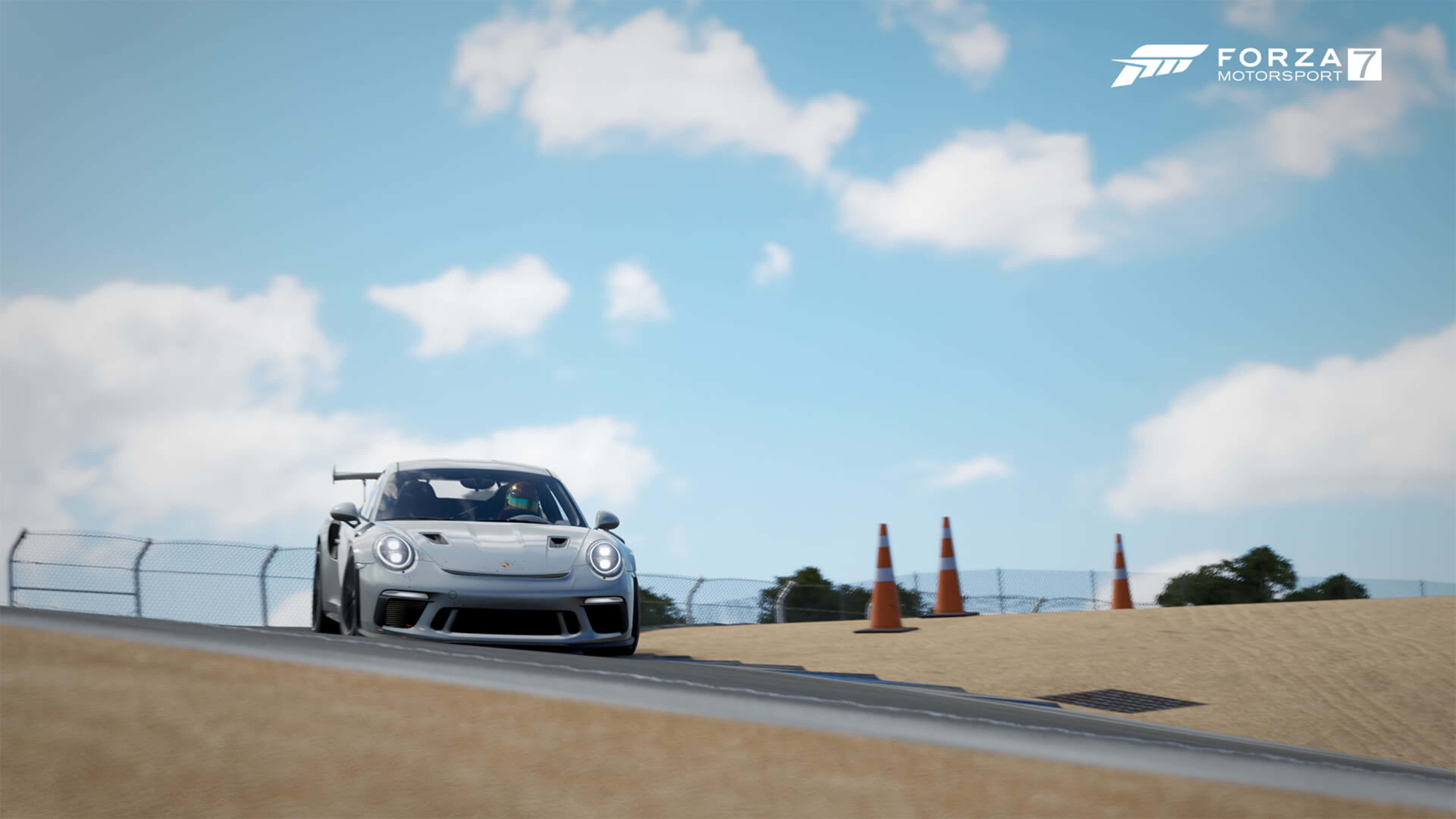 4K《Forza Motorsport 7》背景：銀色 2023 Porsche 911 壁紙 — 一輛銀色保時捷 GT3 RS 在晴朗藍天和蓬鬆白雲下的沙漠賽道上飛馳。