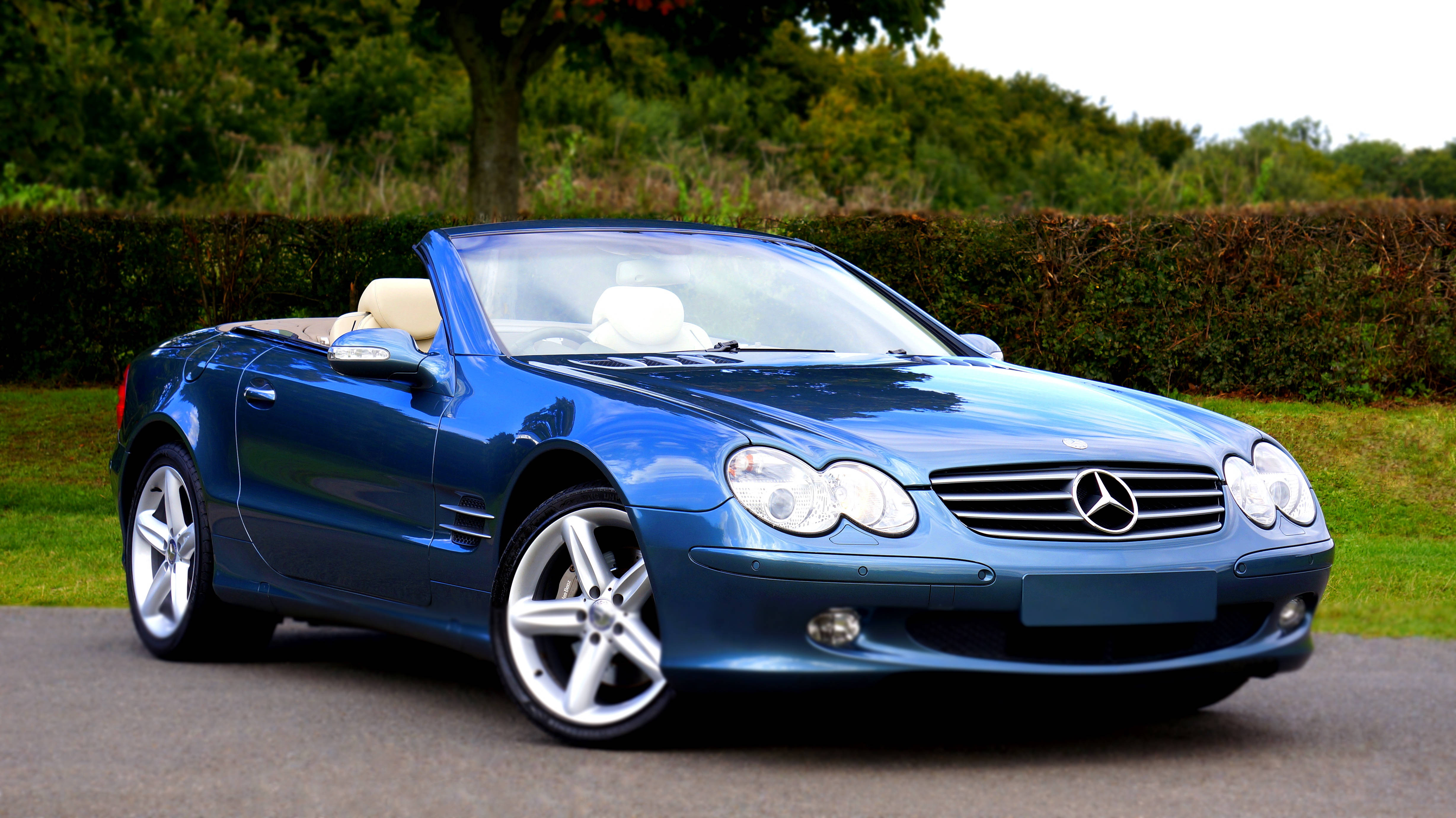 賓士4K藍色敞篷 壁紙 — 一架時尚的藍色 Mercedes SLR McLaren 開篷跑車停泊在鋪砌的道路上，背景有綠色樹籬和樹木。