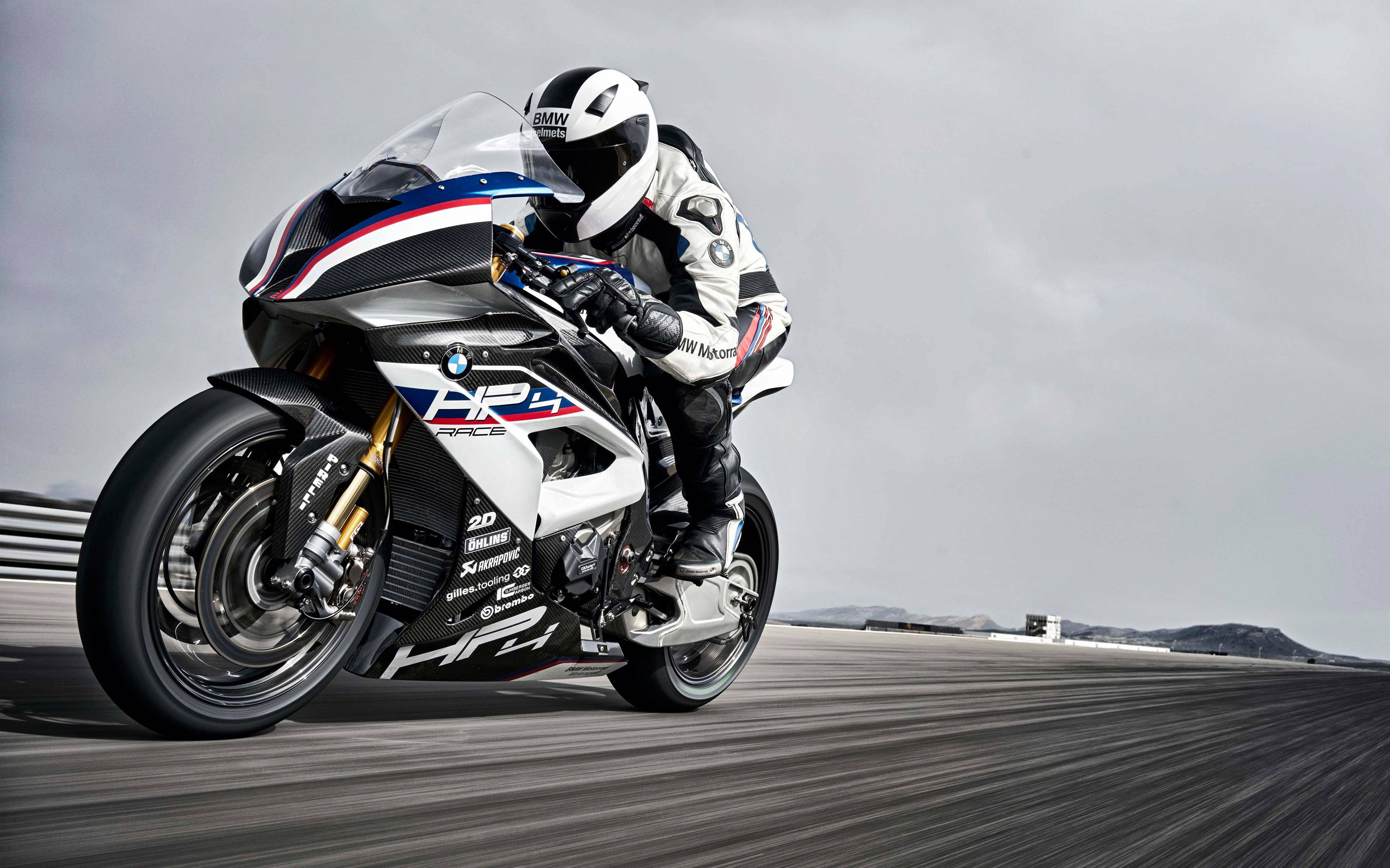 4K HP4賽車摩托車 壁紙 — 一名車手在陰天下的賽道上，騎著白色、藍色和紅色的BMW HP4 Race電單車傾斜入彎。