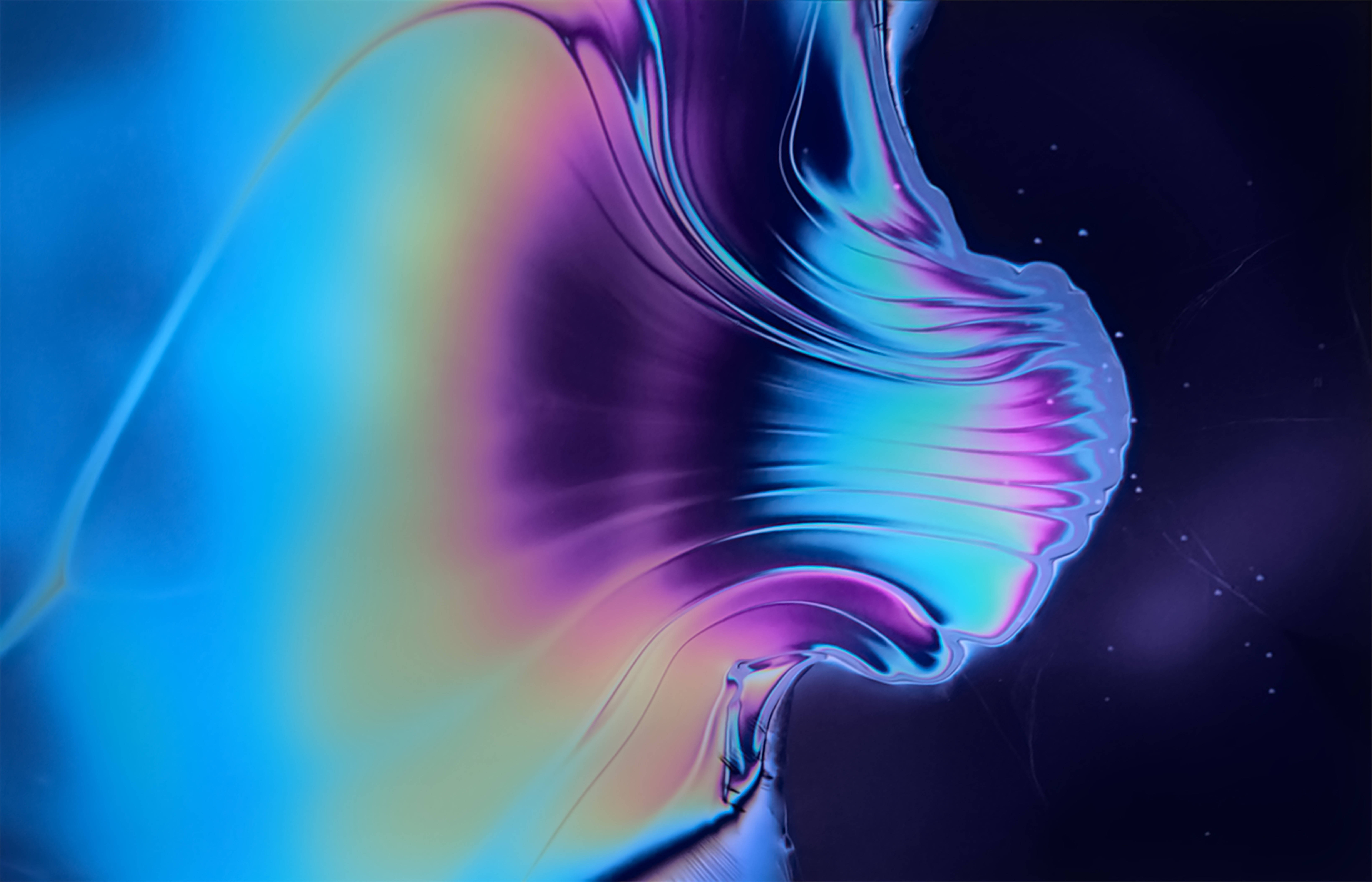 沉浸式 4K iMac 顯示器，搭配流動金屬粉紅與藍色抽象背景 壁紙 — 充滿活力的彩虹色液體在黑暗的宇宙背景下，伴隨著發光的粒子，以平滑起伏的波浪流動。