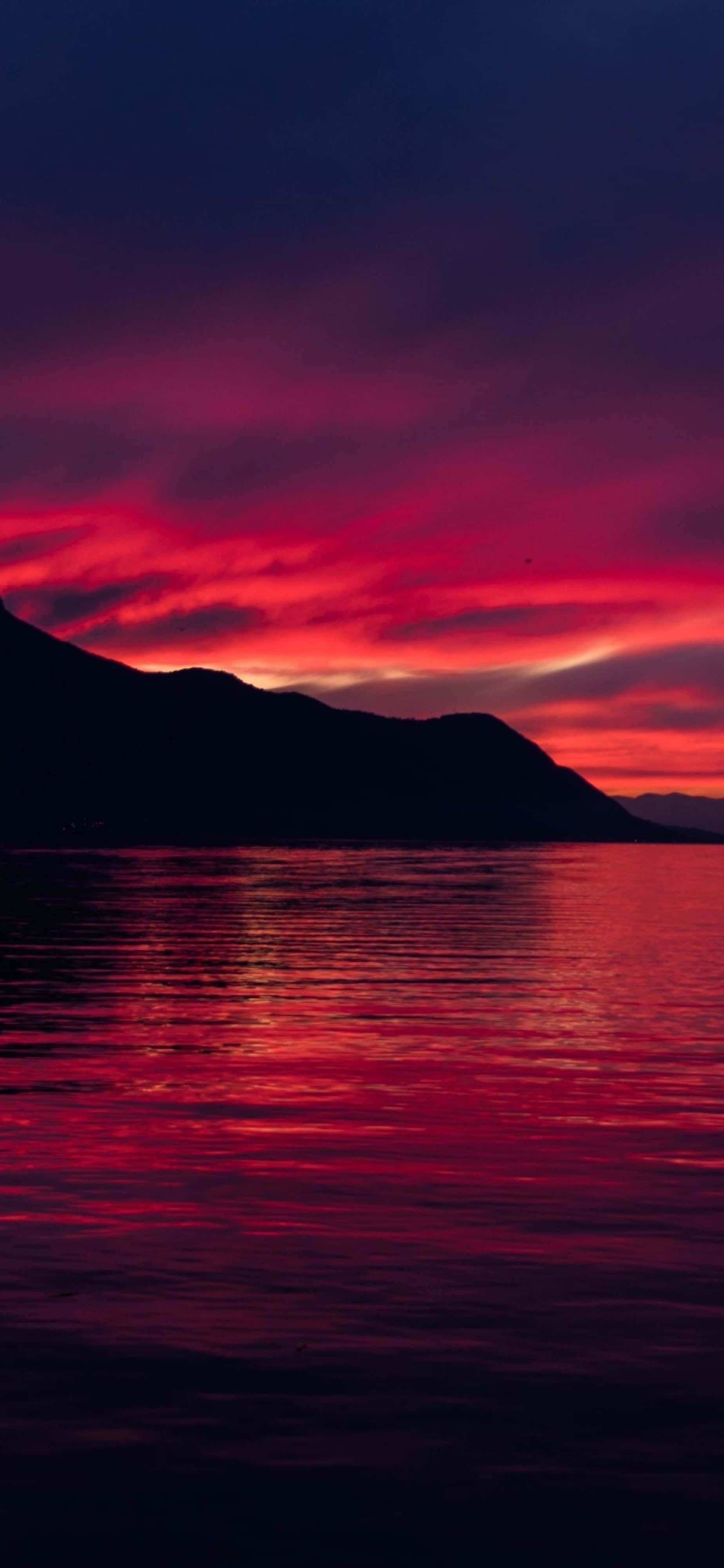 4K iPhone 紅天自然風景 壁紙 — 戲劇性的日落將天空和水面染成火紅和紫色，黑暗的山脈在剪影中聳立。