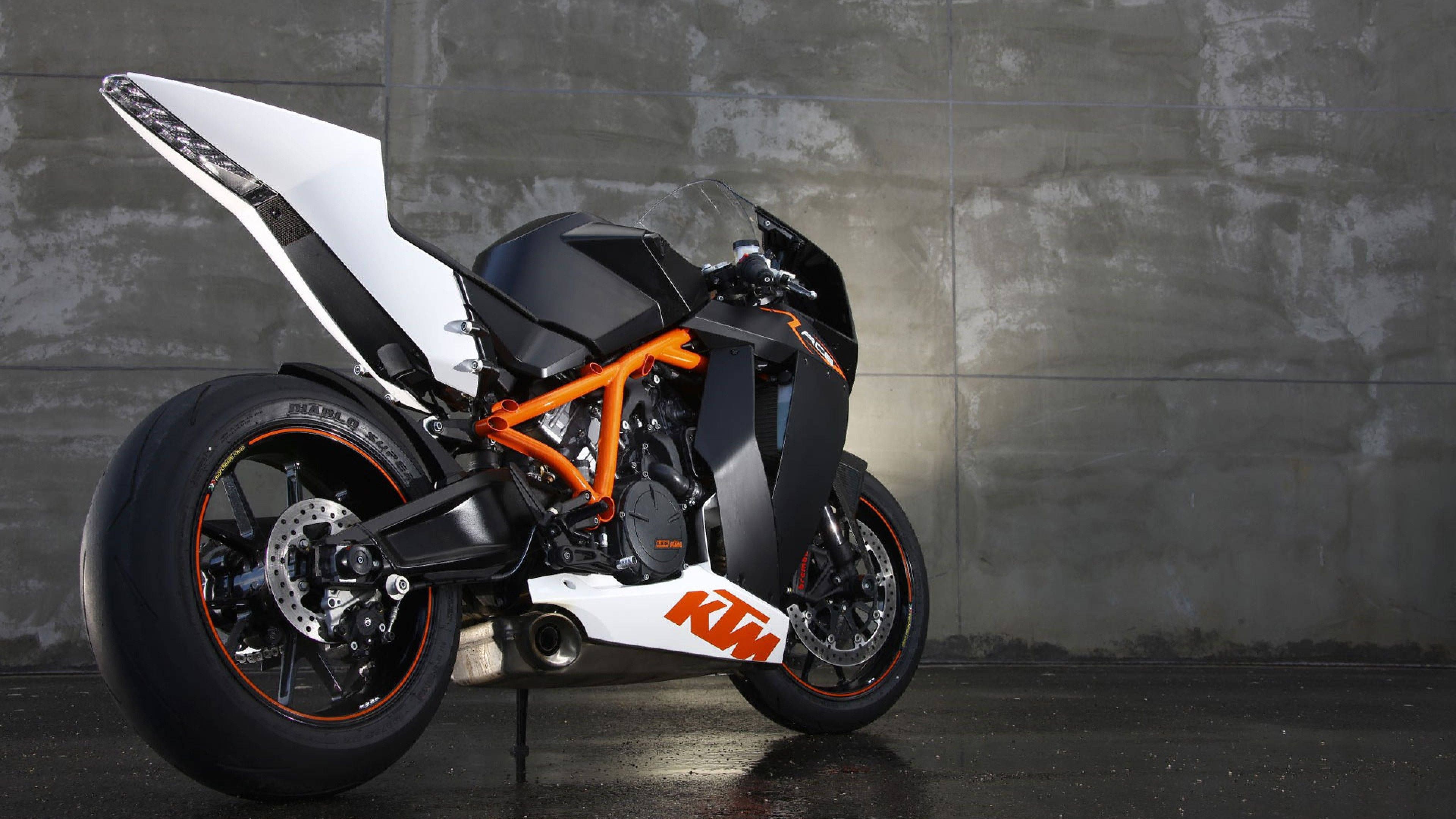 4K KTM Rc8r自行車 壁紙 — 一台時尚的KTM超級摩托車，配備橙色車架和白色車身，矗立在紋理灰色混凝土牆前。