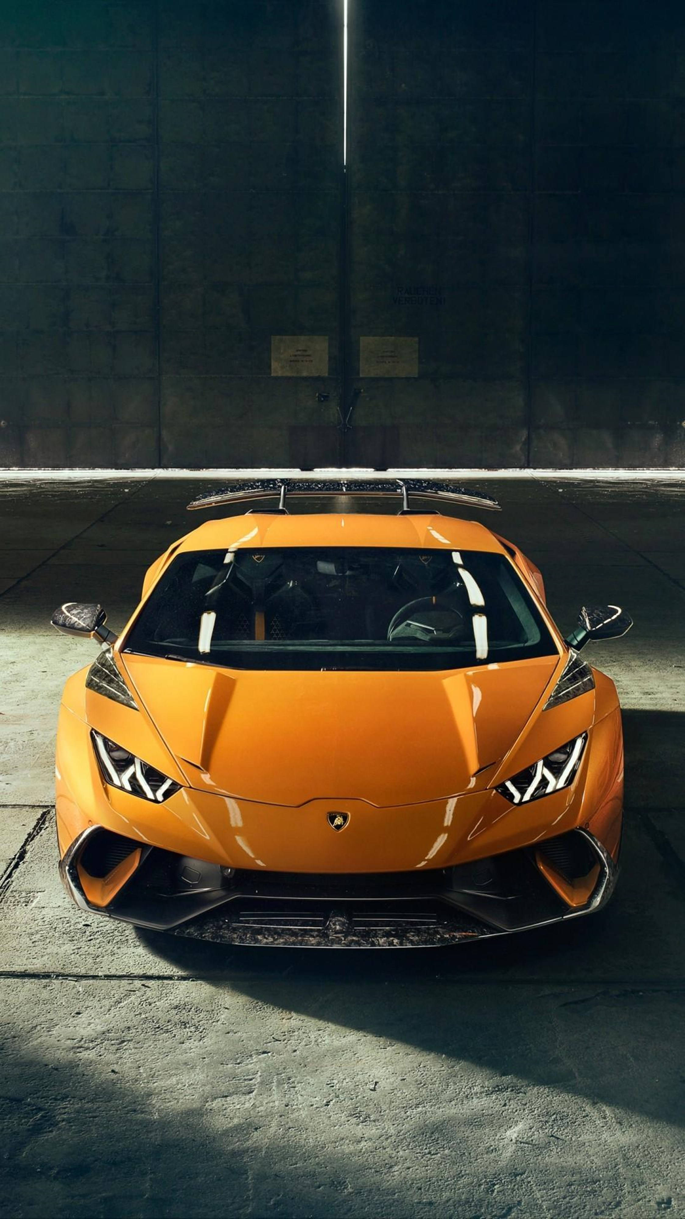 極致時尚的4K Lamborghini智慧手機 壁紙 — 一輛充滿活力的橙色林寶堅尼跑車在空蕩蕩的混凝土車庫中，在一盞頭頂燈下閃閃發光。