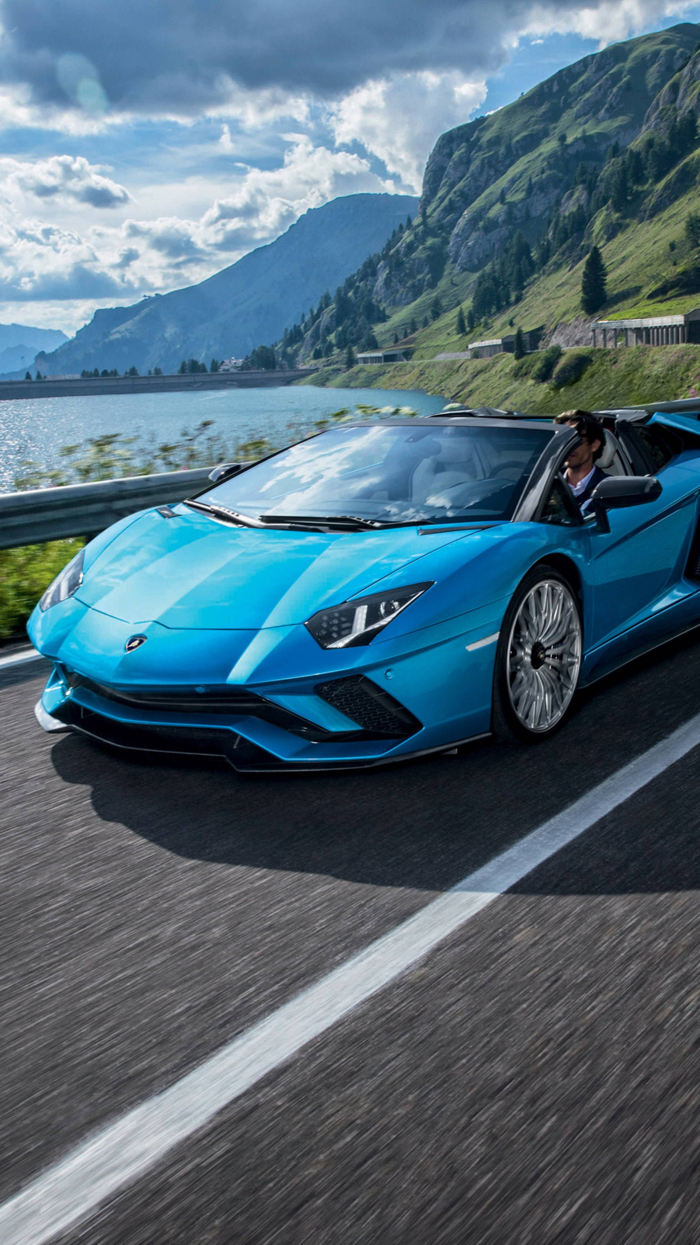4K Lamborghini iPhone 配景風光 壁紙 — 一輛充滿活力的藍色林寶堅尼Aventador開篷跑車，在部分多雲的天空下，沿著湖邊的山路飛馳。
