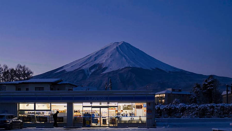便利店 4K Lo Fi 壁紙 — 喺深藍色嘅暮色天空下，白雪覆蓋嘅富士山聳立喺燈火通明嘅Lawson便利店後面。