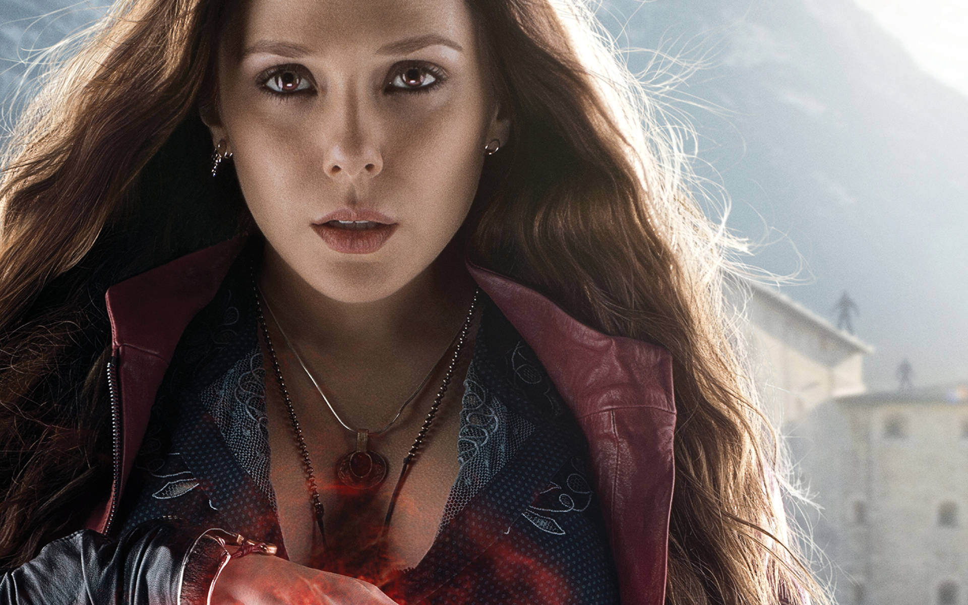 緋紅女巫近照 4K 馬克 Marvel 蘋果手機壁紙 壁紙 — 一位兇猛的女超級英雄，擁有飄逸的棕色頭髮和從胸口散發出的發光紅色能量，背景是山脈。