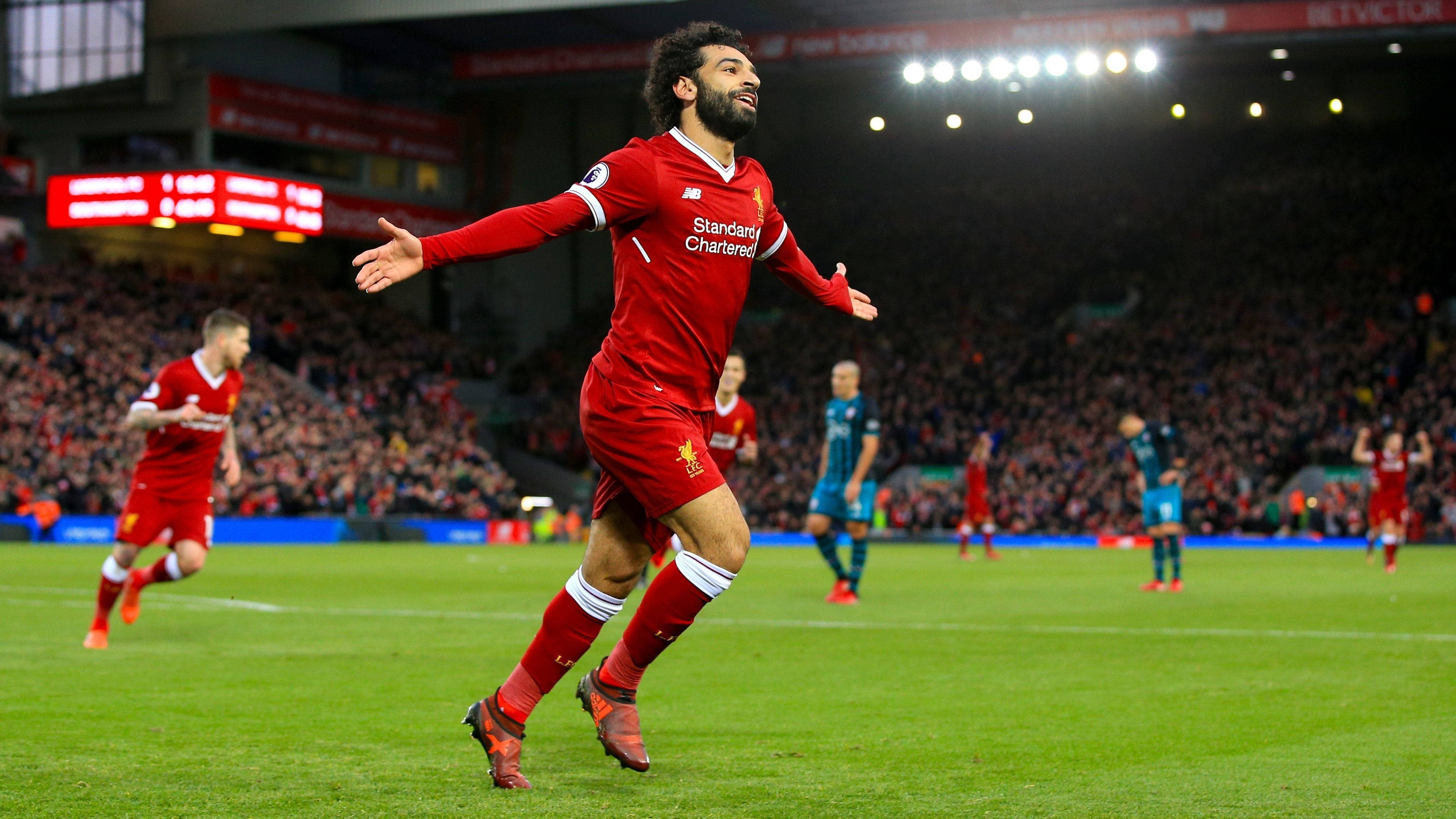 4K 足球 Mohamed Salah 壁紙 — 一名身穿紅色球衣的利物浦足球員在燈光璀璨的球場上張開雙臂慶祝入球。