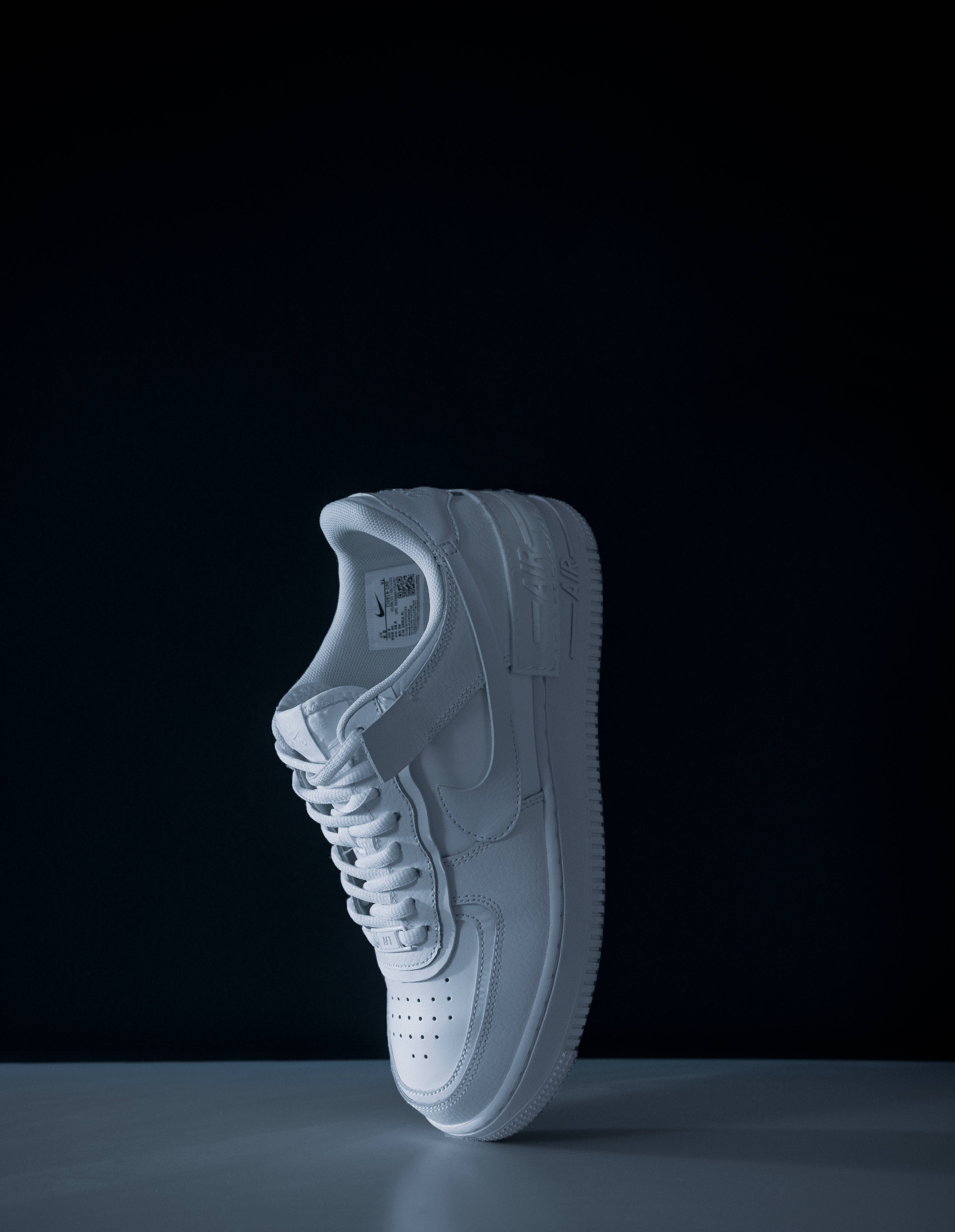 4K Nike 鞋觸地 壁紙 — 一雙純白運動鞋直立於深黑色背景前，柔和的工作室燈光照射其上。