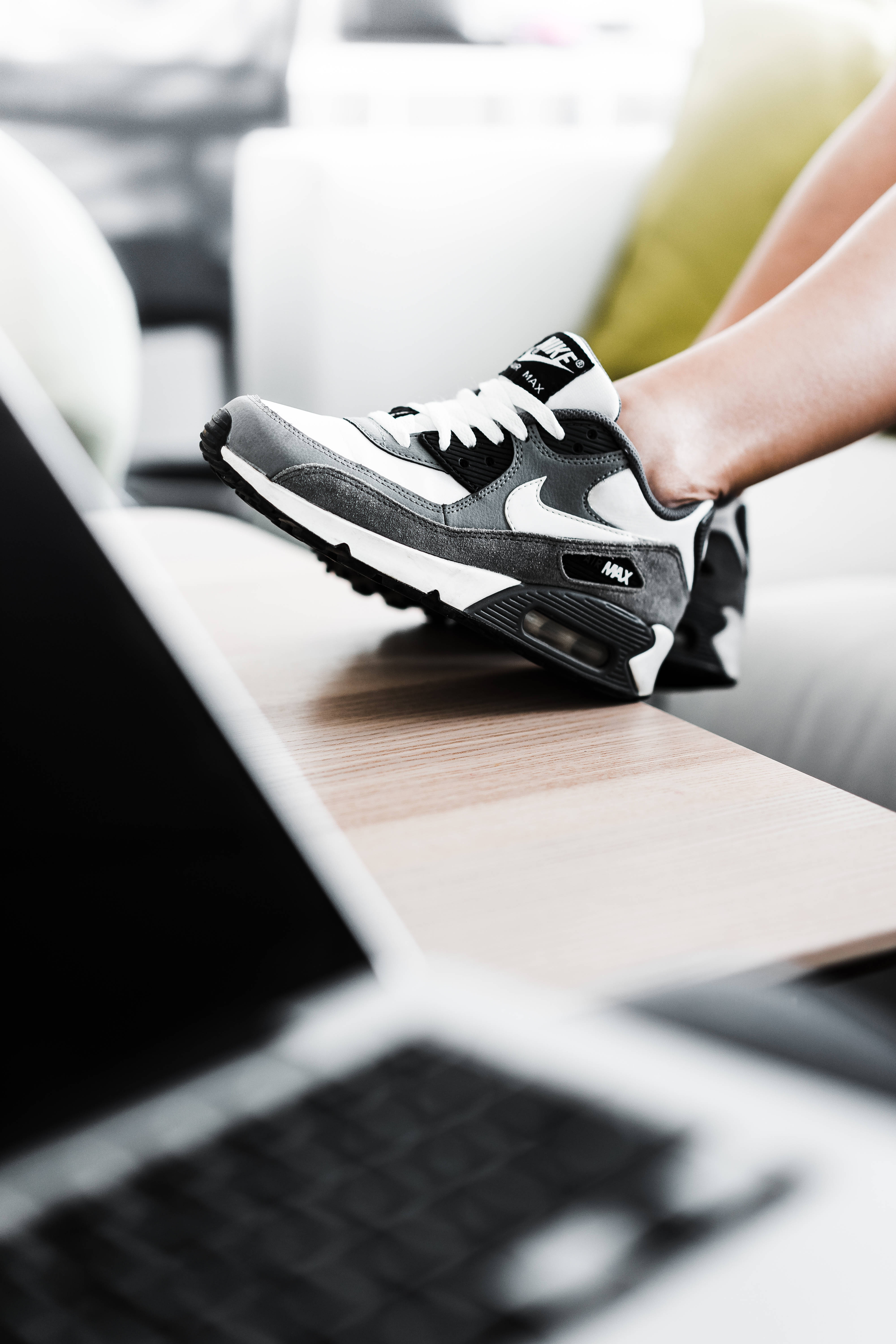 4K Nike 黑色鞋履置於桌面 壁紙 — 一個人的腳穿著黑白Nike Air Max運動鞋，擱在現代客廳的木桌上，旁邊放著一部打開的筆記本電腦。