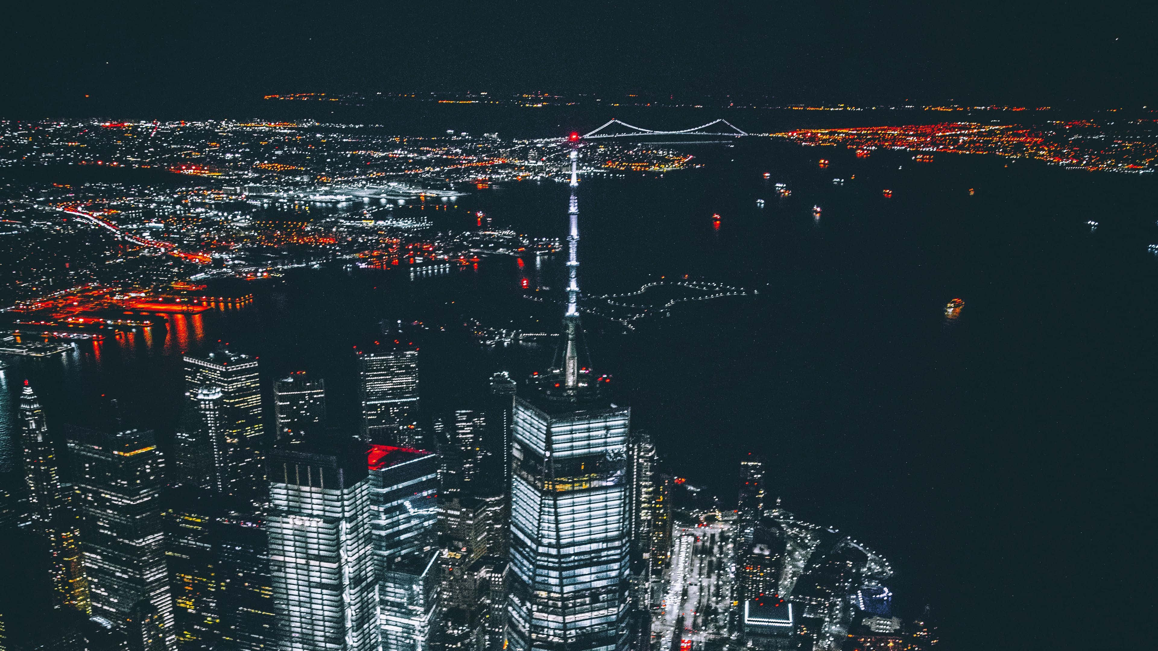 4K 紐約市夜間帝國大廈 壁紙 — 夜晚空中俯瞰閃爍的城市景觀，燈火通明的摩天大樓和橫跨黑暗水面的發光橋樑。