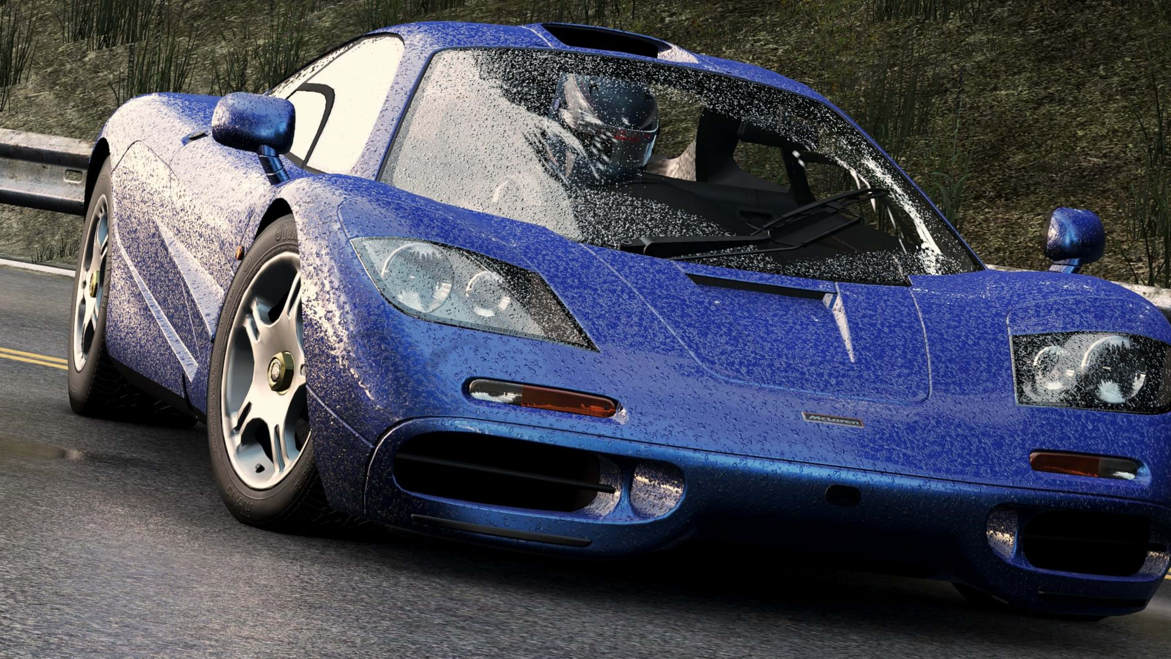 4K Project Cars 藍色麥拉倫 F1 LM 背景 壁紙 — 一輛充滿活力的藍色McLaren F1跑車濺滿水珠，在潮濕的道路上疾馳，車內可見戴頭盔的司機。
