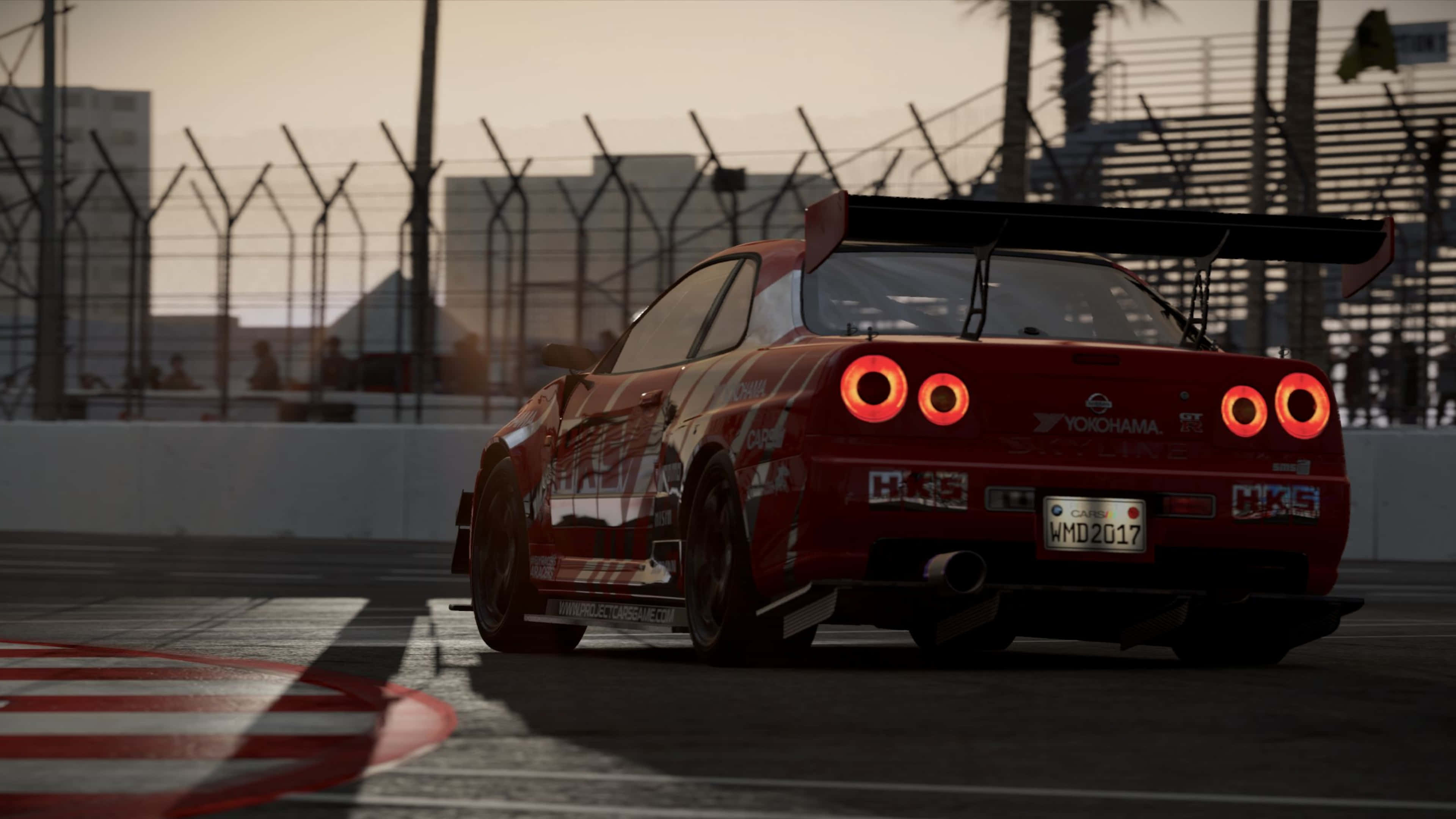 4K Project Cars 紅色 Nissan Skyline GTR R34 背景 壁紙 — 一輛紅色日產Skyline賽車在日落時分，以發光的尾燈在賽道上飛馳，背景有棕櫚樹和圍欄。