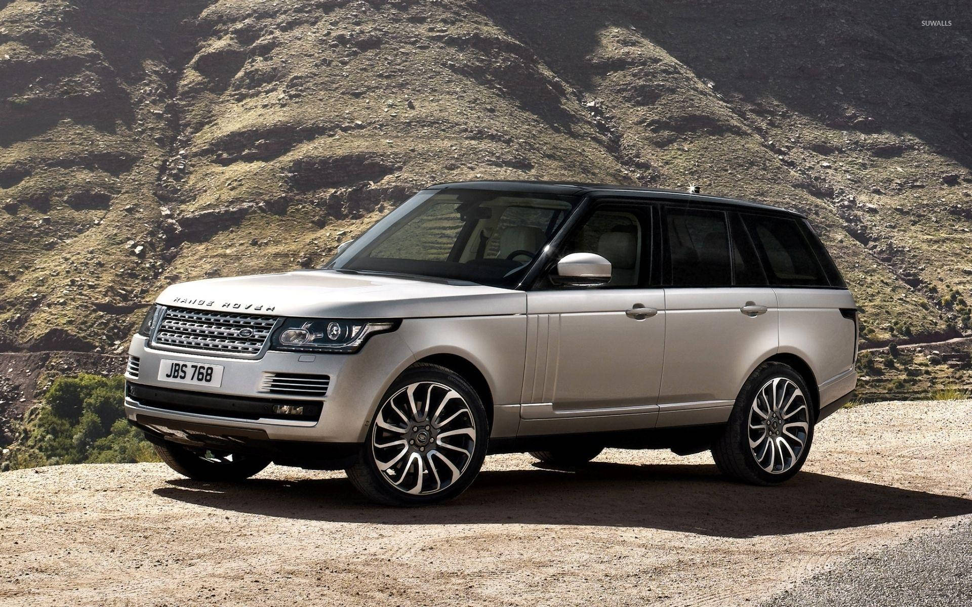 銀色Range Rover SUV停在山路上，後面有山丘。