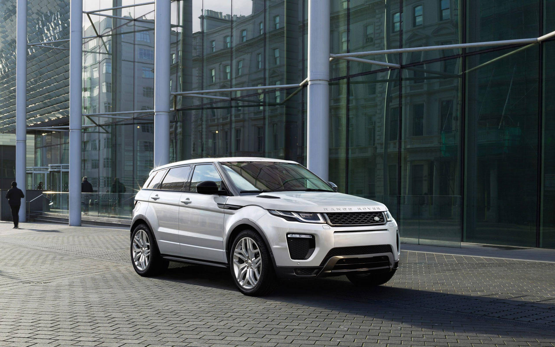 銀色 Range Rover Evoque 停泊在玻璃建築前，附近有行人走過。