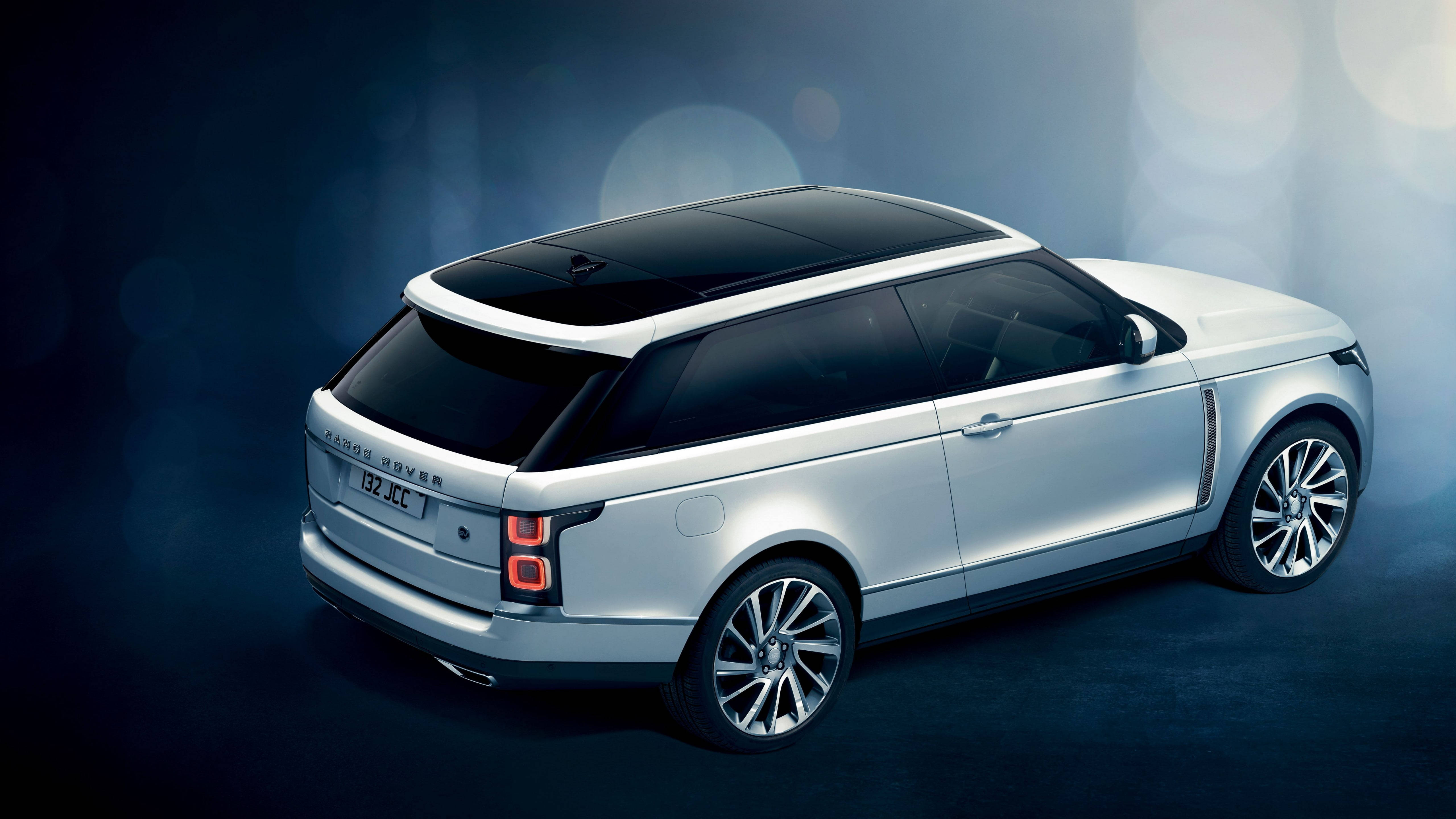 4K 范圍 Rover 俯瞰圖 壁紙 — 時尚的銀色 Range Rover SUV 在戲劇性的工作室燈光下，在深藍色背景上散發著散景亮點。