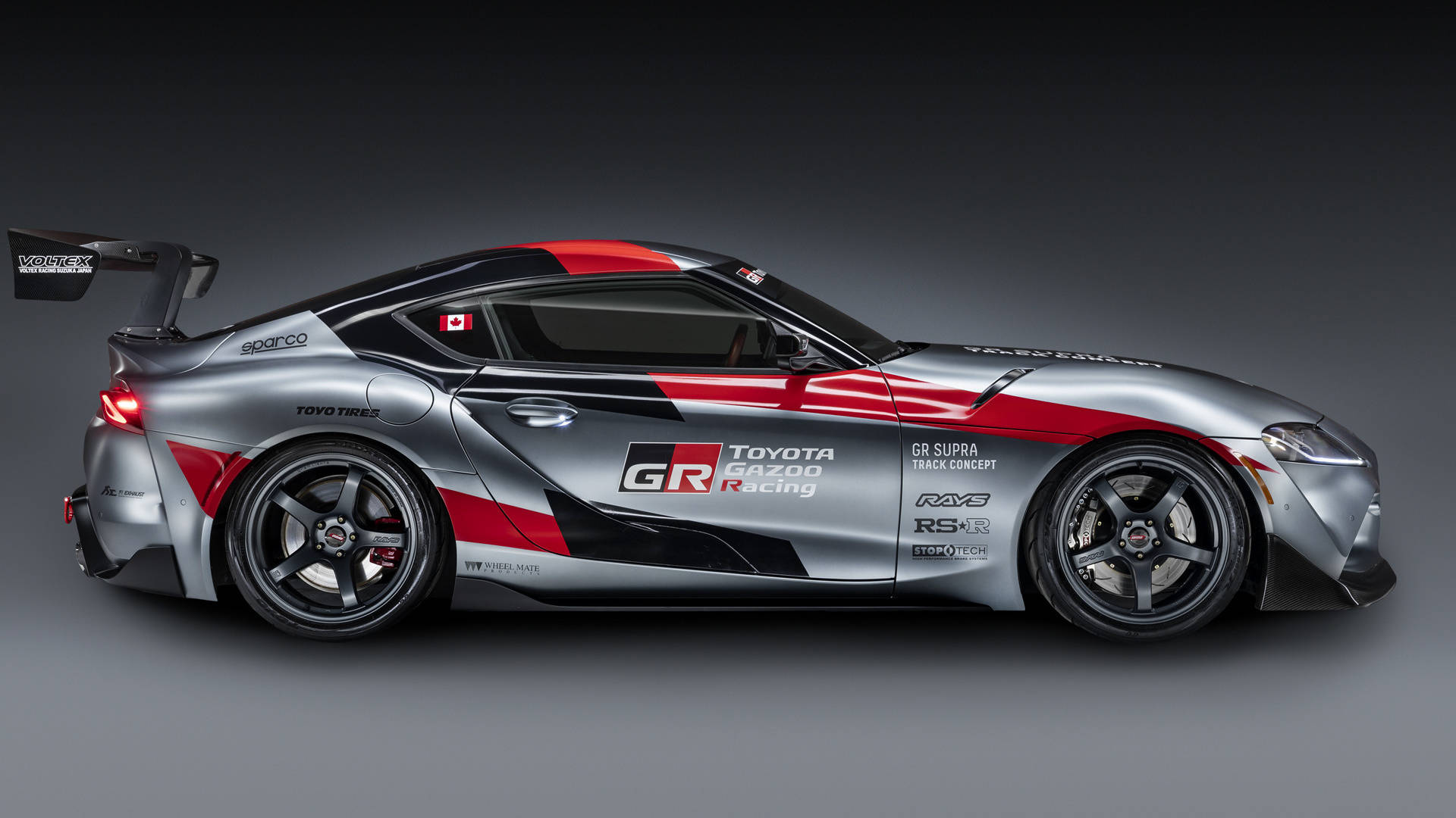 4K 丰田Supra 灰色賽車版 壁紙 — 在工作室燈光下展示的時尚銀紅雙色豐田GR Supra賽車概念車，帶有黑色飾邊和贊助商貼紙。