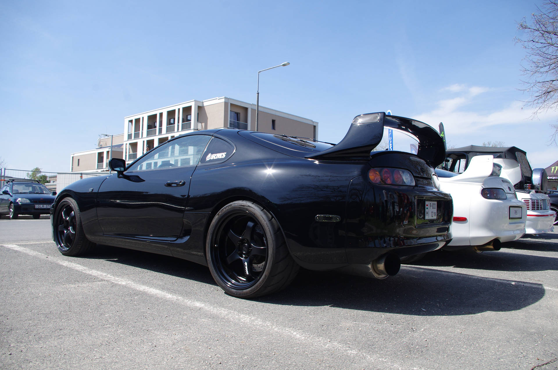 黑色豐田Supra，尾翼升起，停泊在陽光普照的城市停車場。